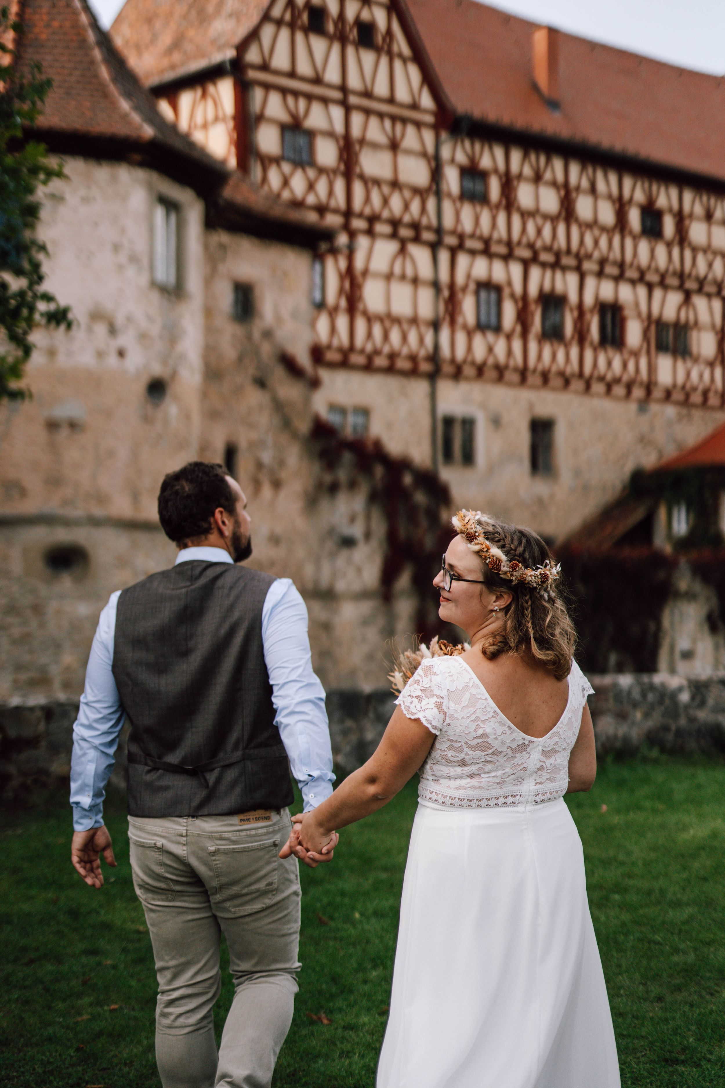 A couple walks hand in hand near a historic half-timbered building.