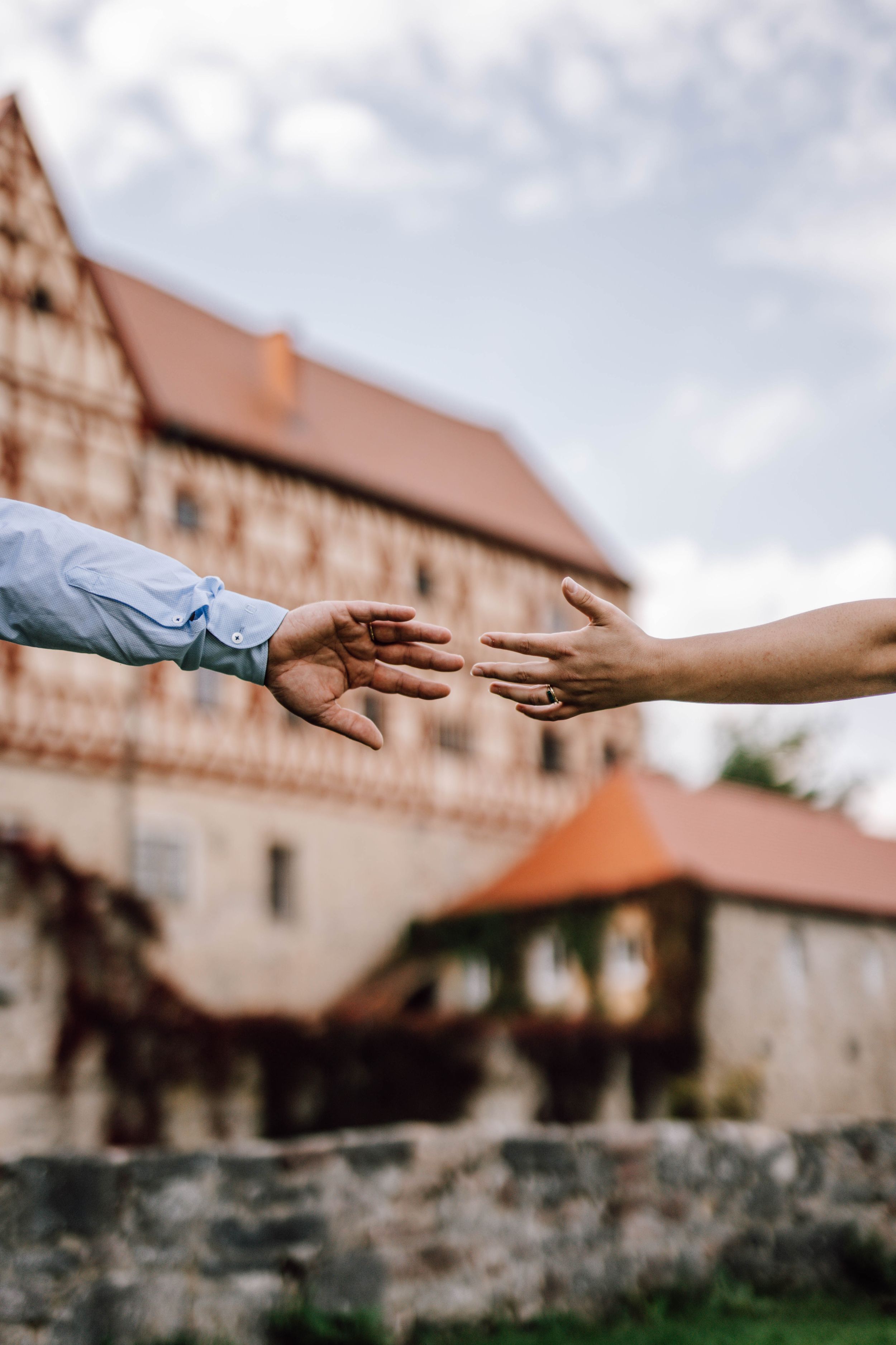 Two hands reaching toward each other with a traditional German building in the background.