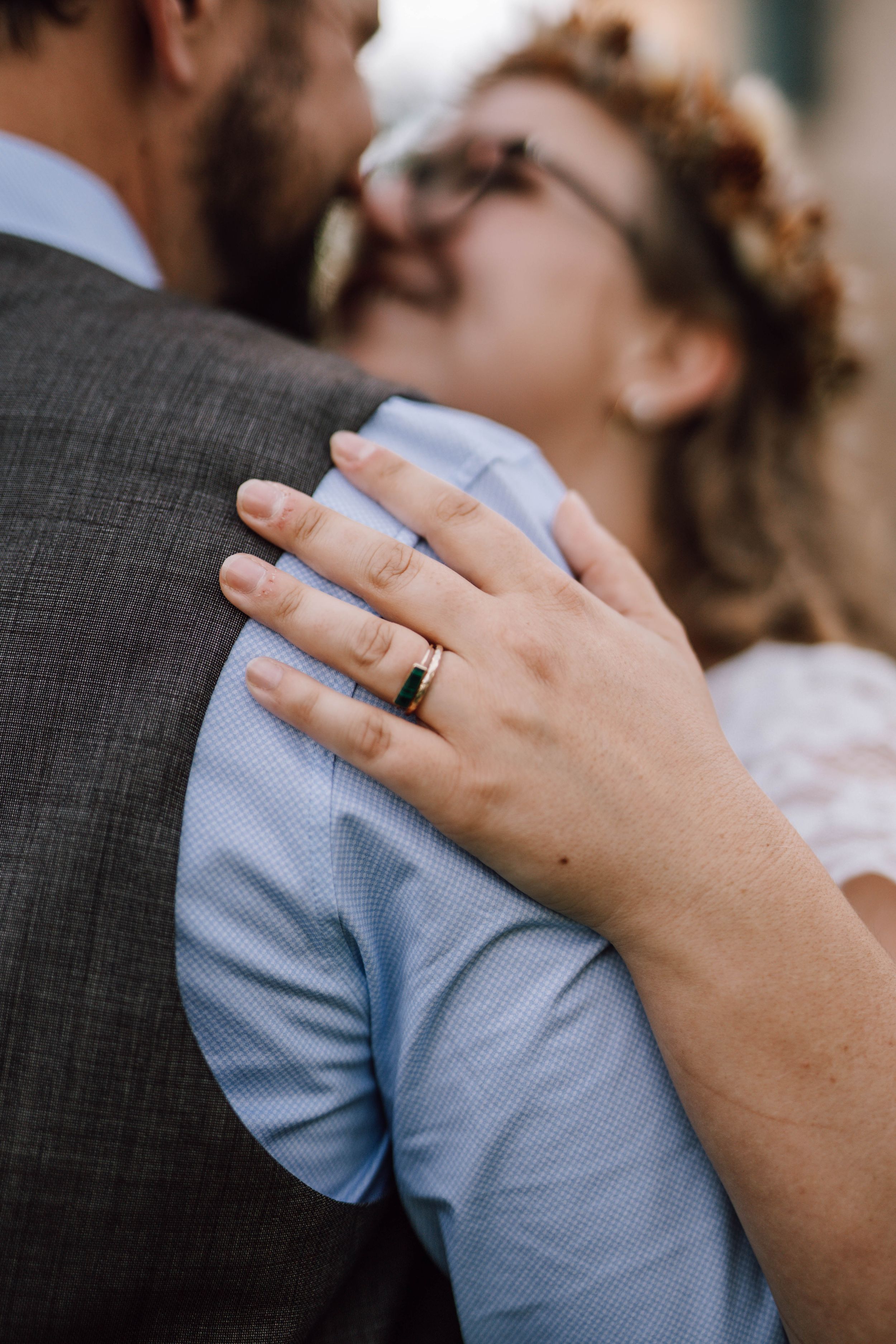 Close-up of hands with wedding rings embracing against a grey couch background.