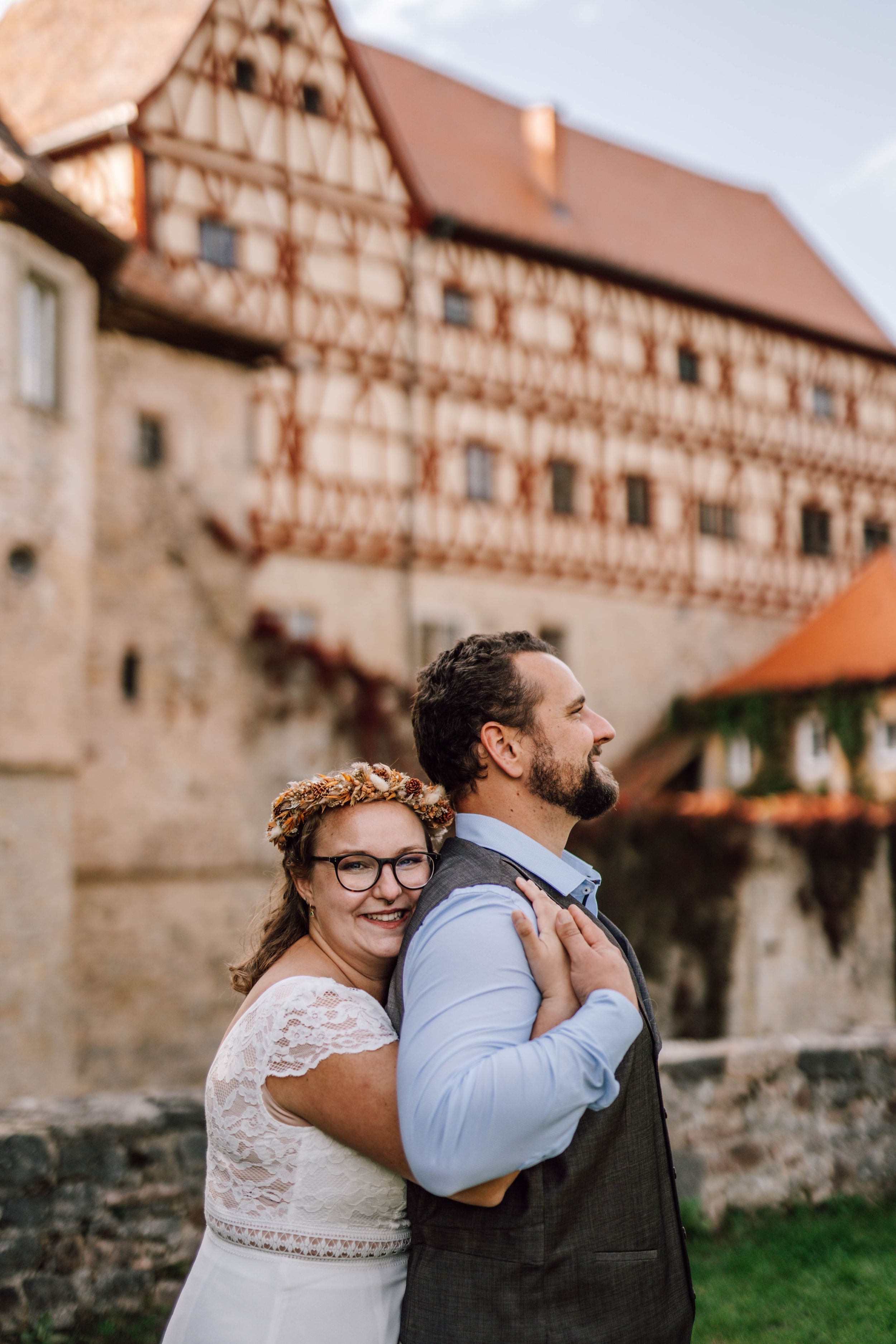 Newlyweds embrace in front of historic half-timbered building during golden hour.
