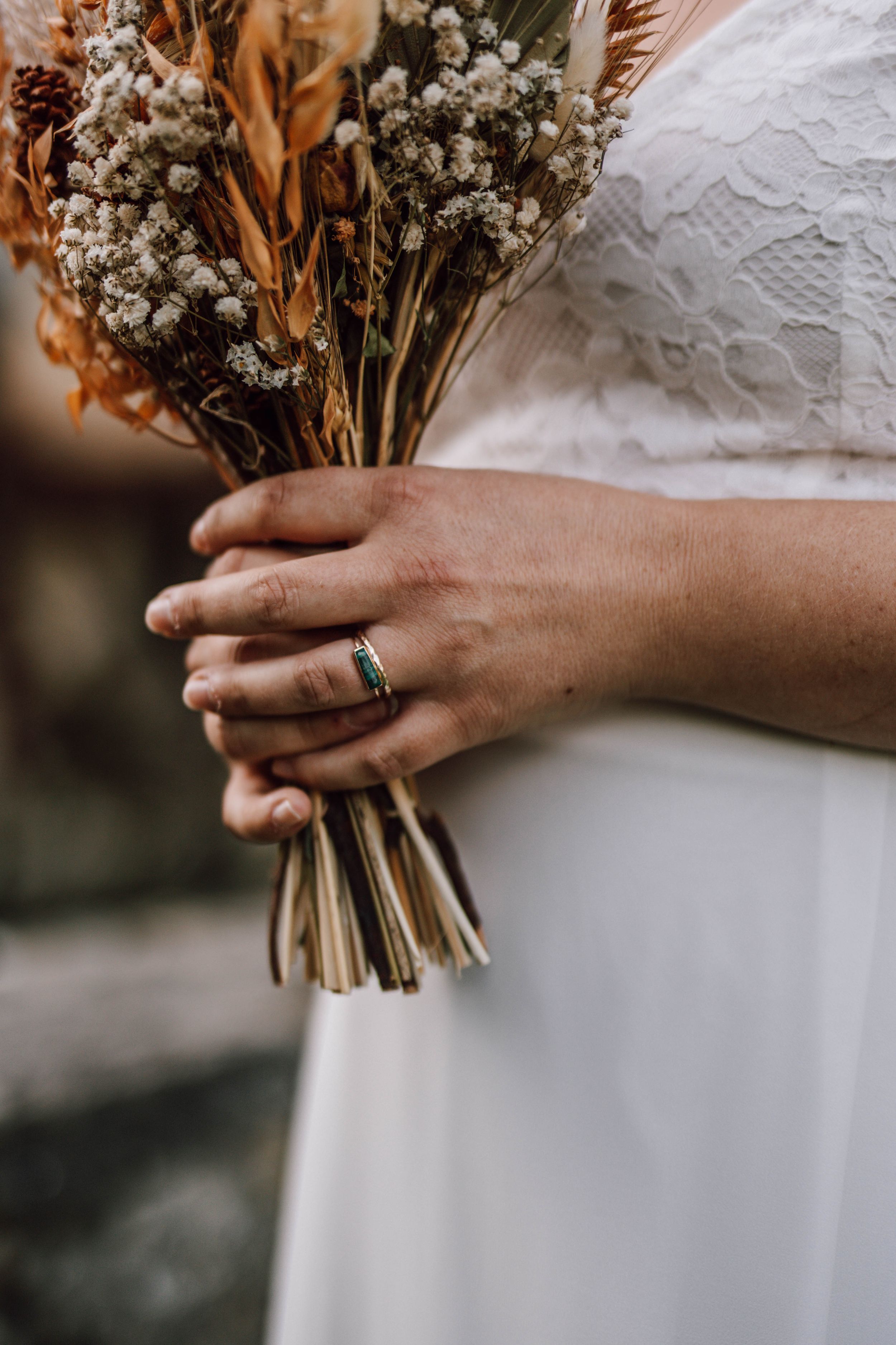 Delicate dried flower wedding bouquet held against white lace dress.