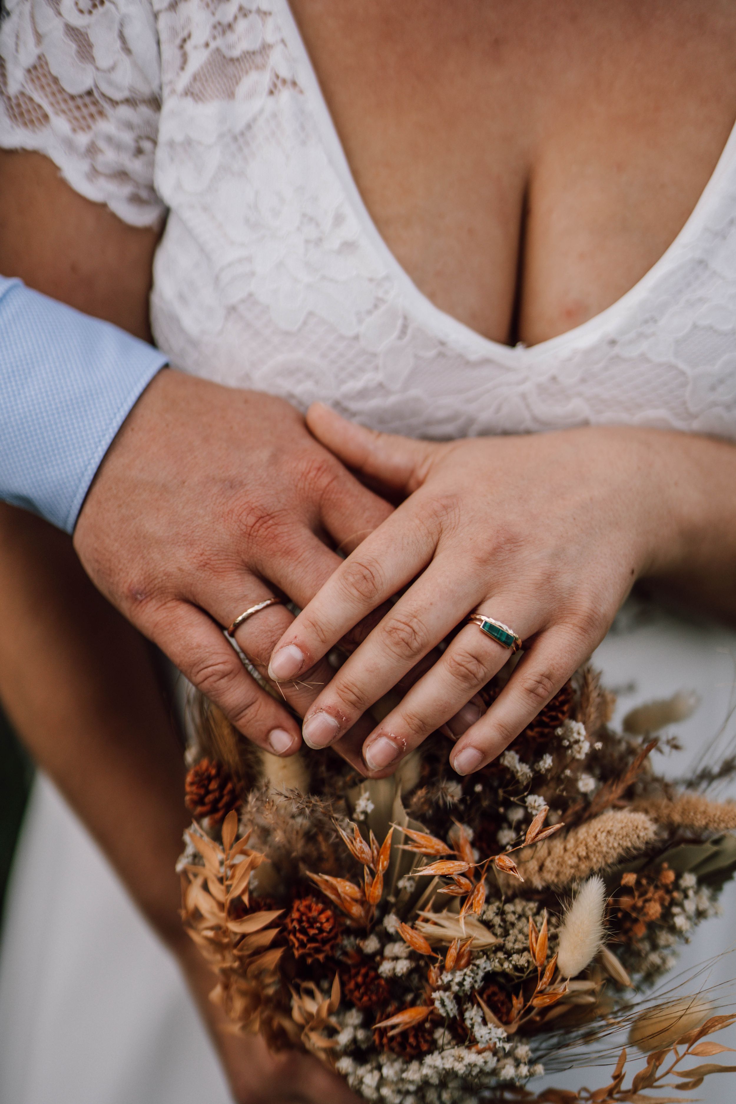 Wedding rings and hands holding rustic dried flower bouquet with lace dress detail.