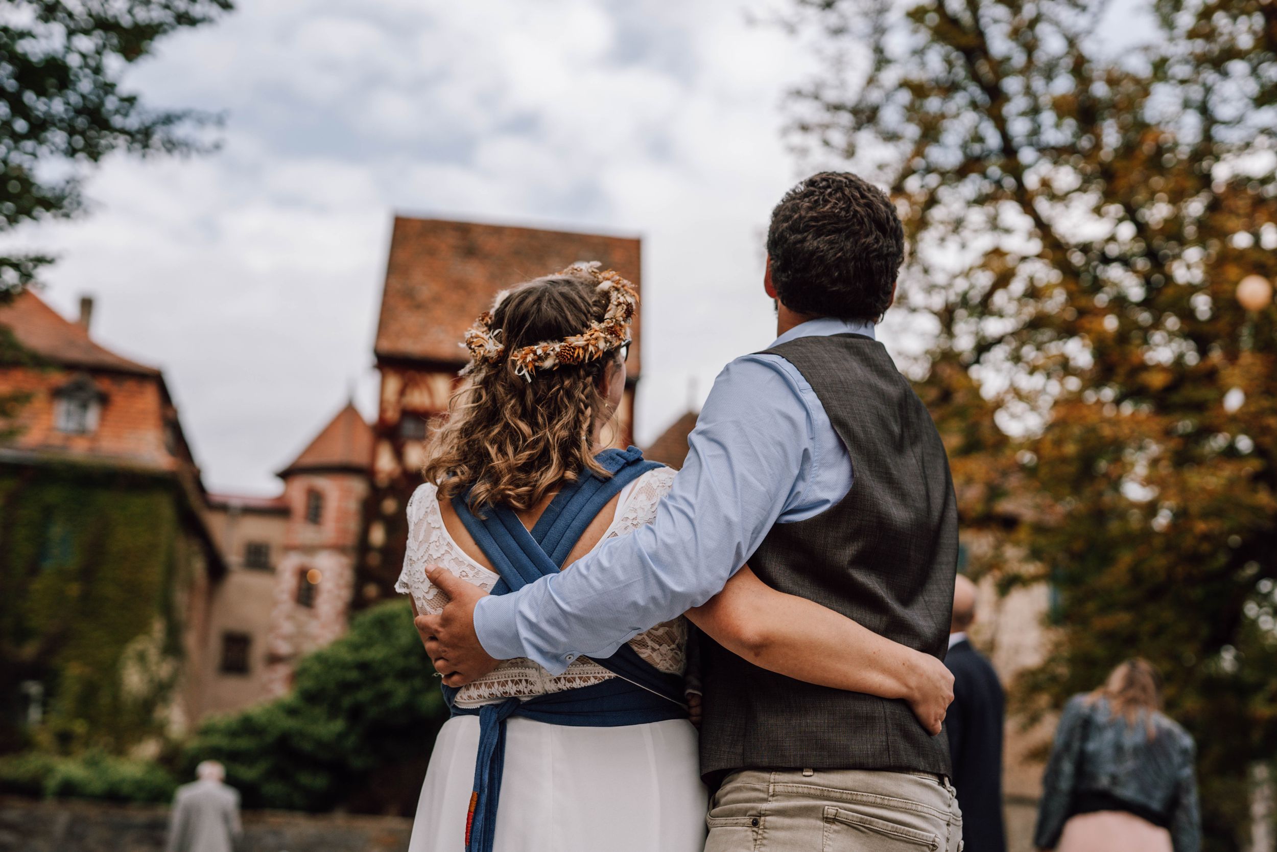 Couple walking along historic stone wall with autumn trees in background.