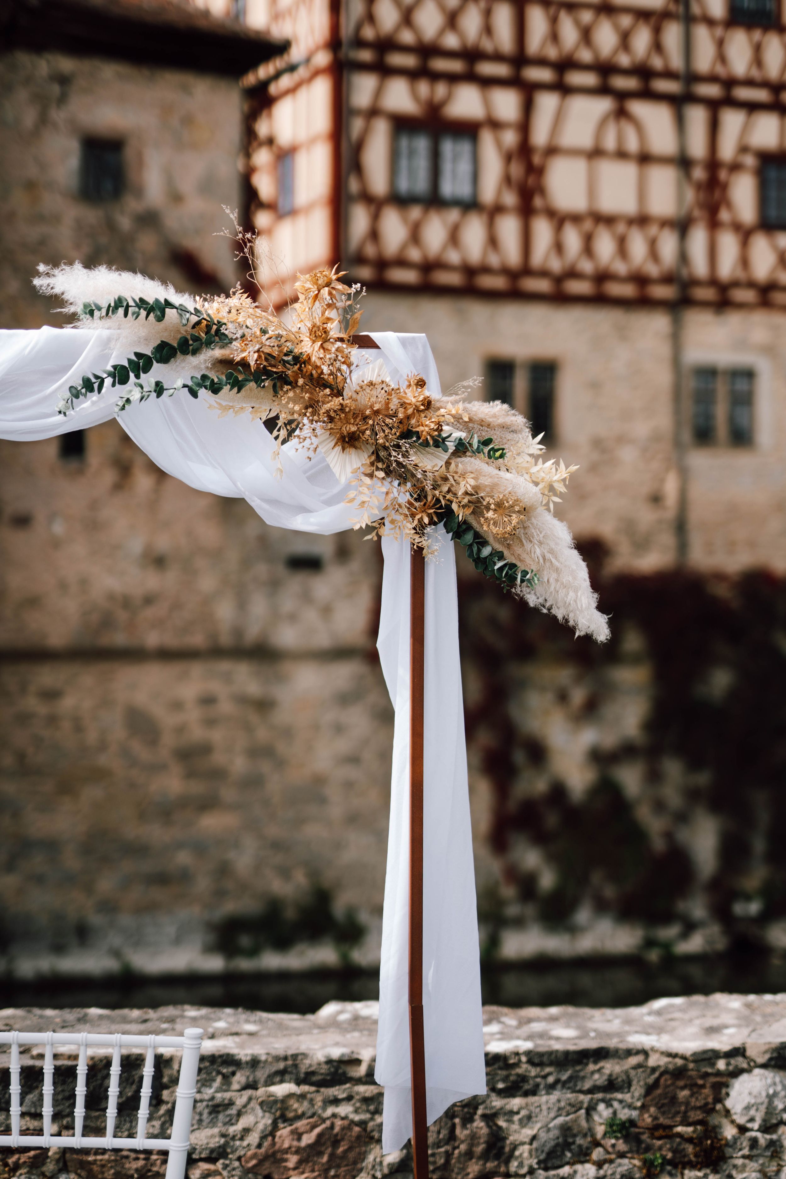 White fabric and dried flowers decorate stone wall with historic building backdrop.