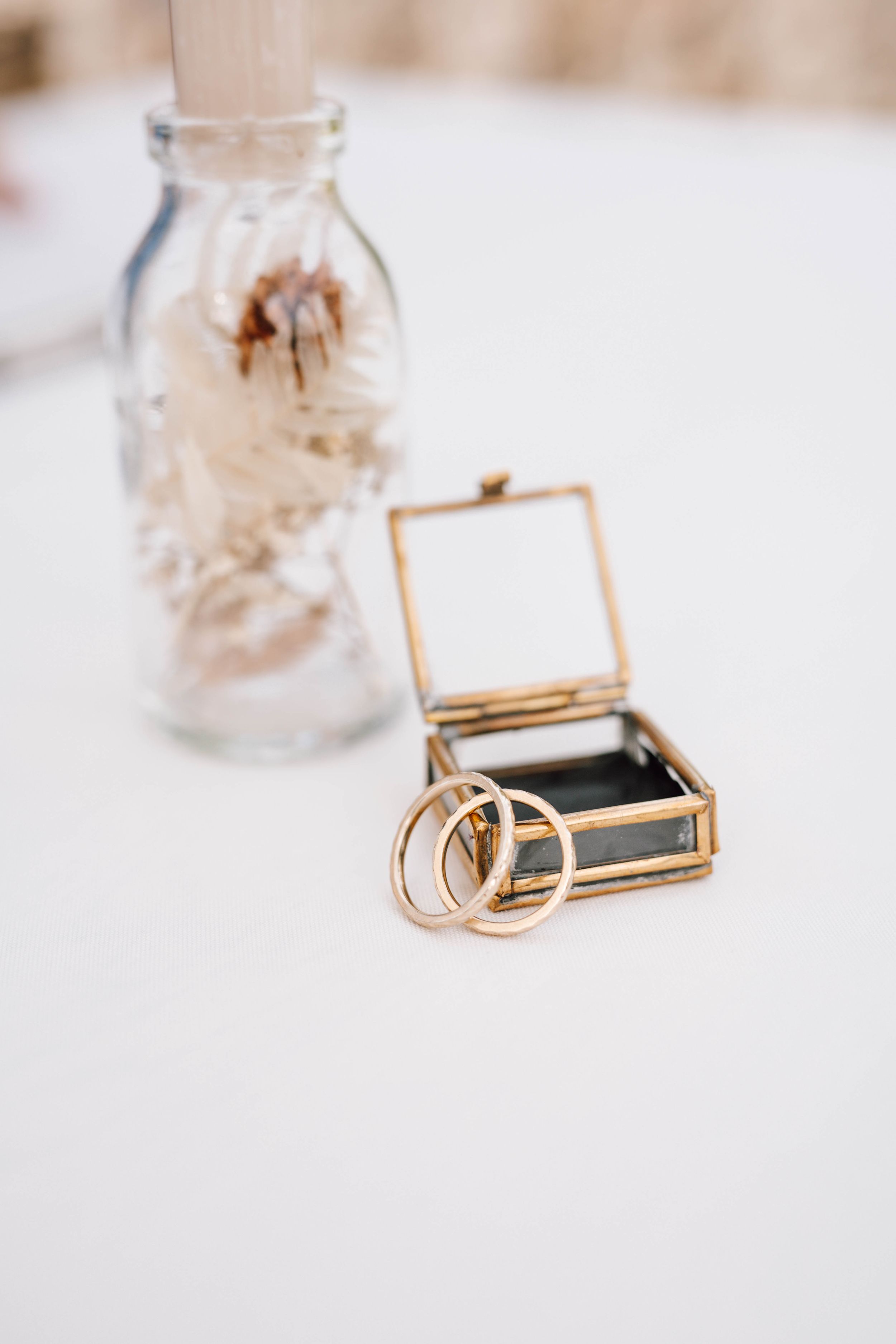 Wedding rings and jewelry displayed in elegant glass containers on white surface.