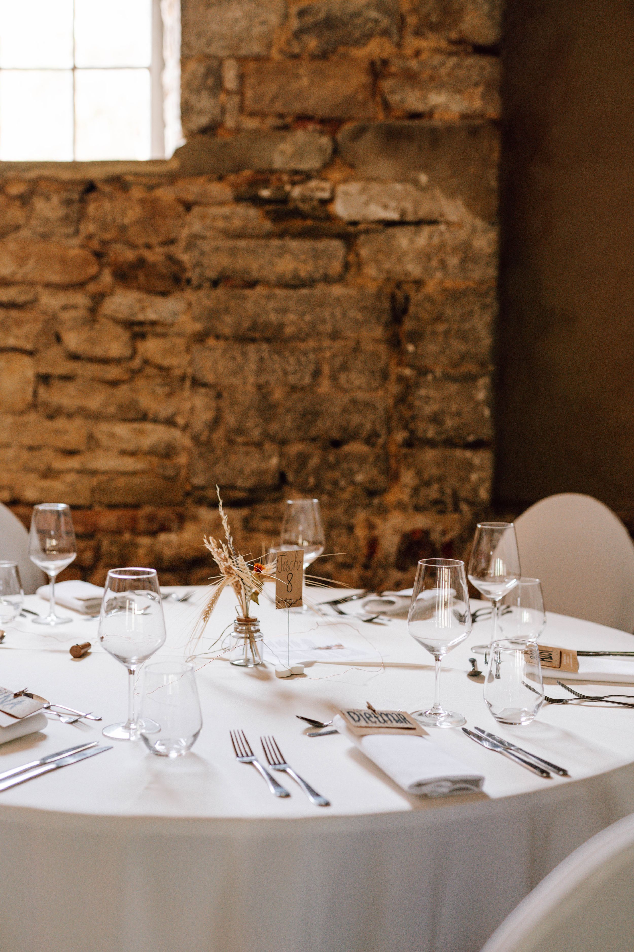Elegant table settings with wine glasses and white linens in a rustic stone-walled venue.
