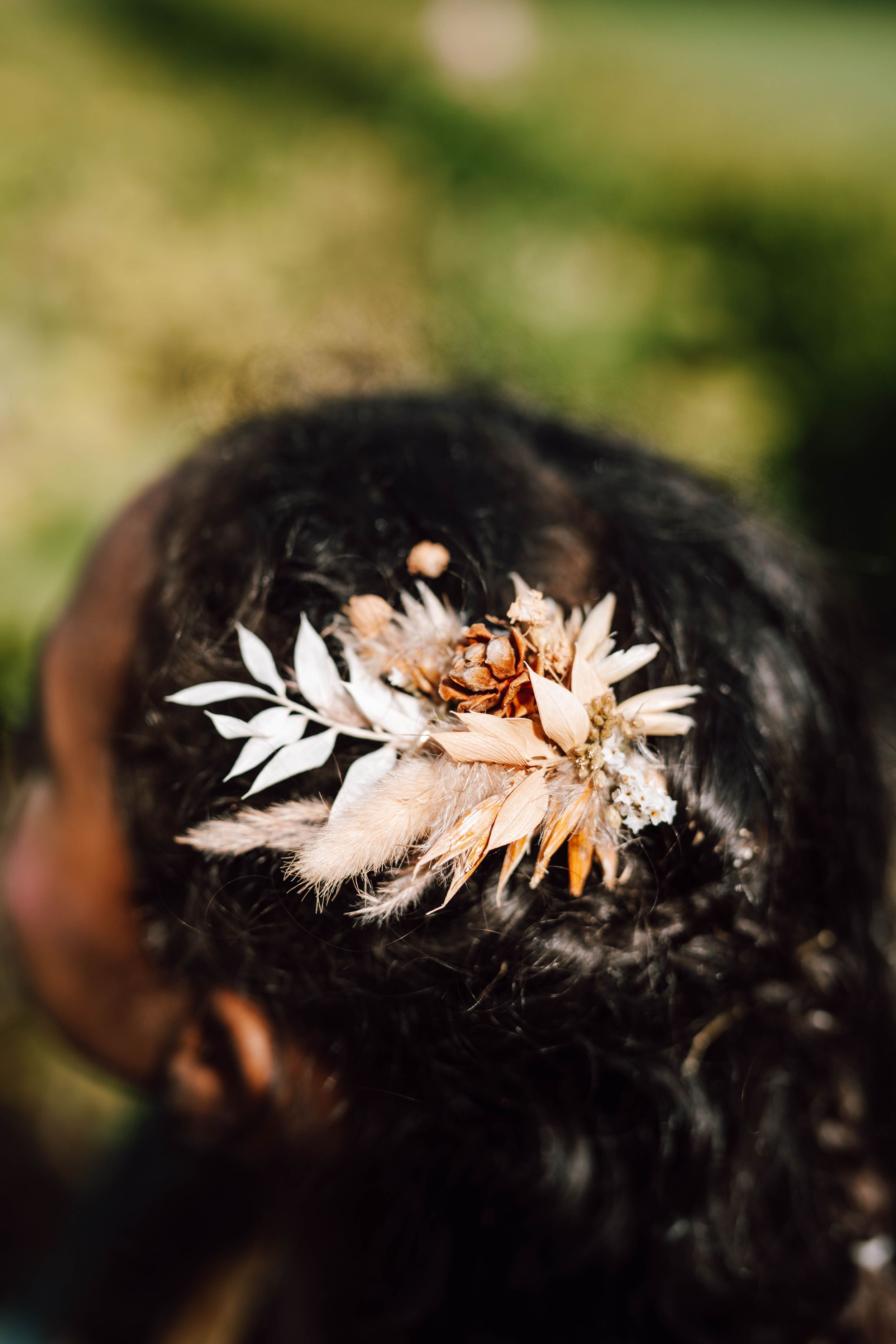 Delicate white feather and floral hair accessory adorns dark hair in a wedding style.
