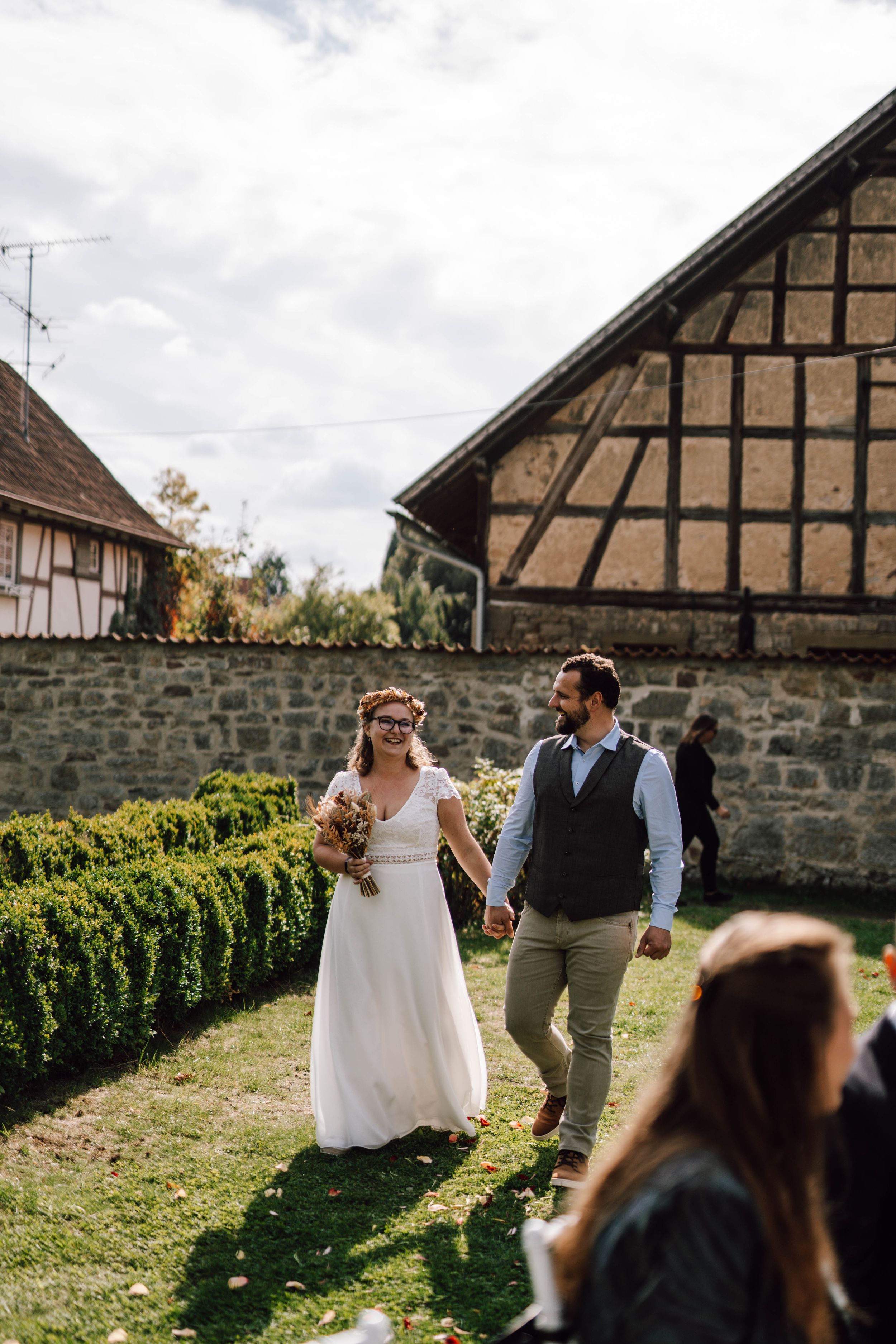 Wedding couple walking through garden with traditional half-timbered houses in background.