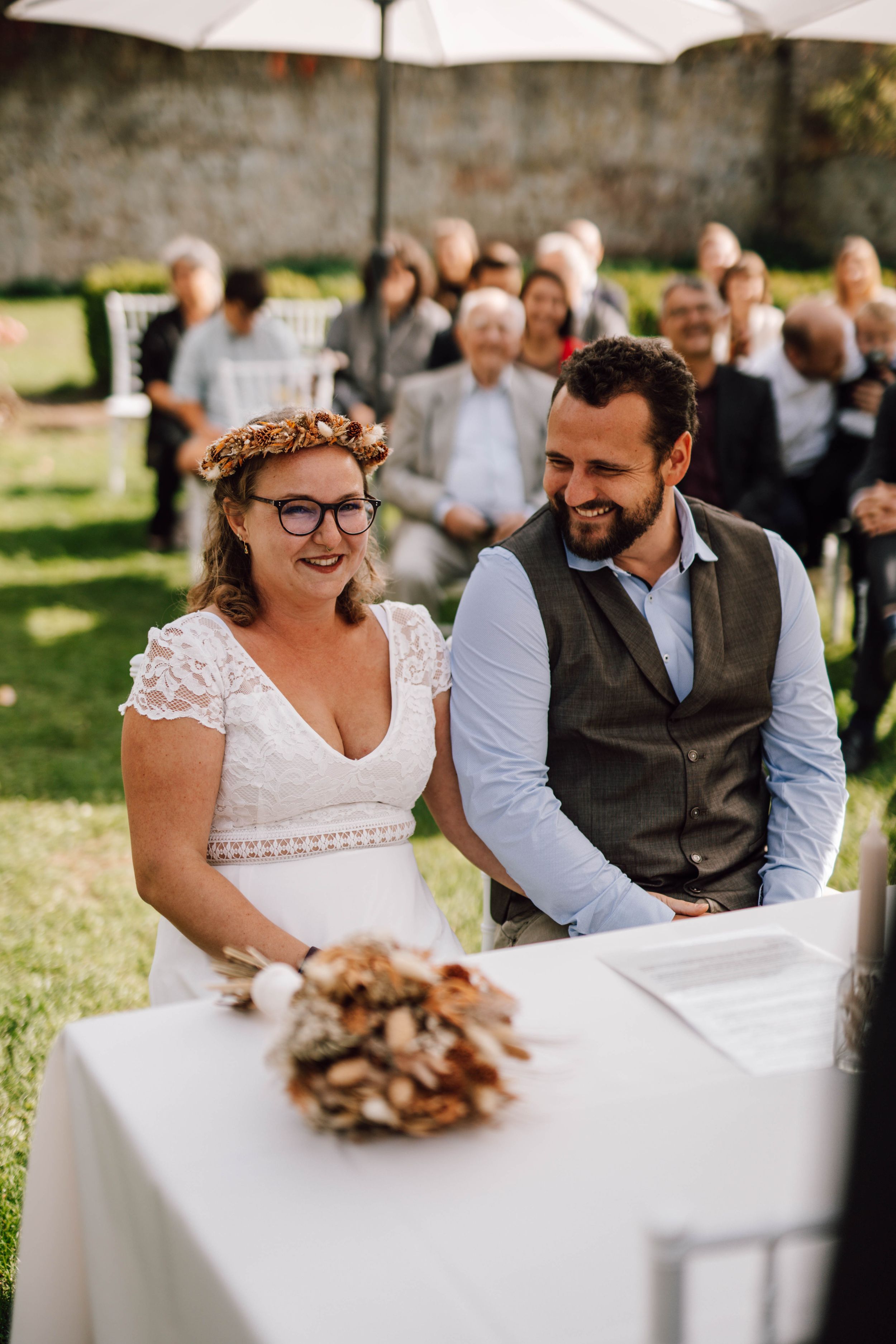 Outdoor wedding ceremony under white umbrellas with couple seated at signing table.