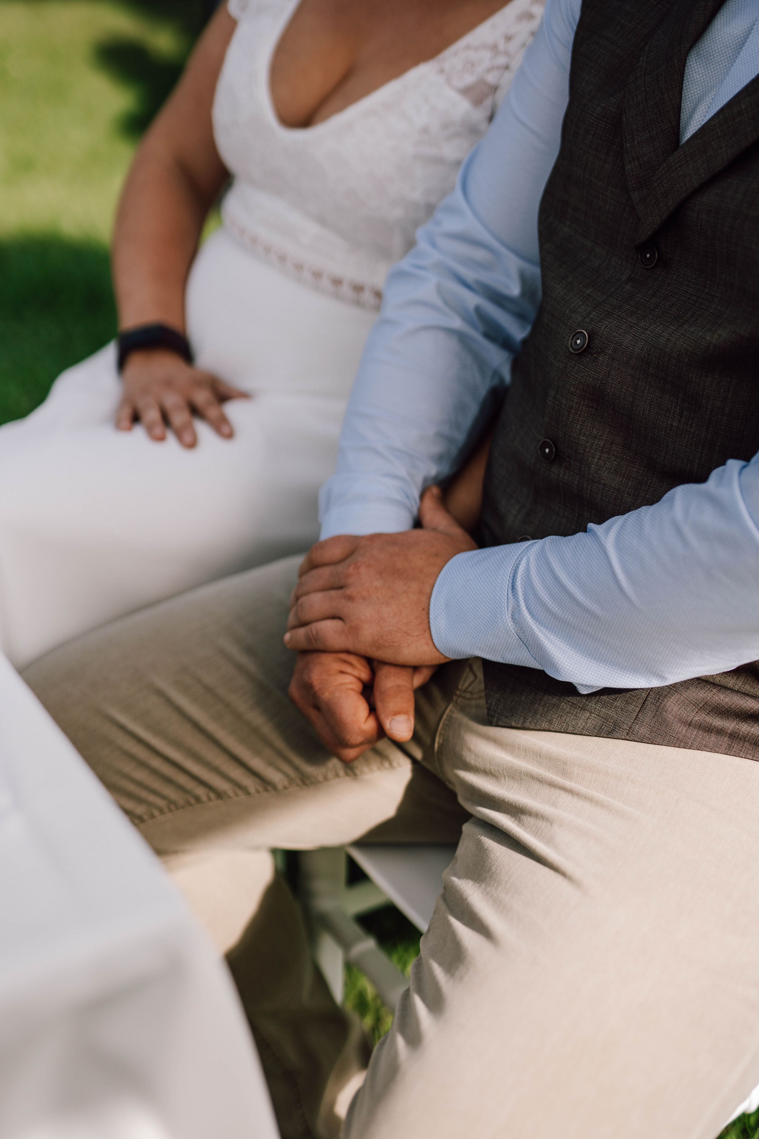 Close-up of wedding couple's hands resting on white and khaki attire.
