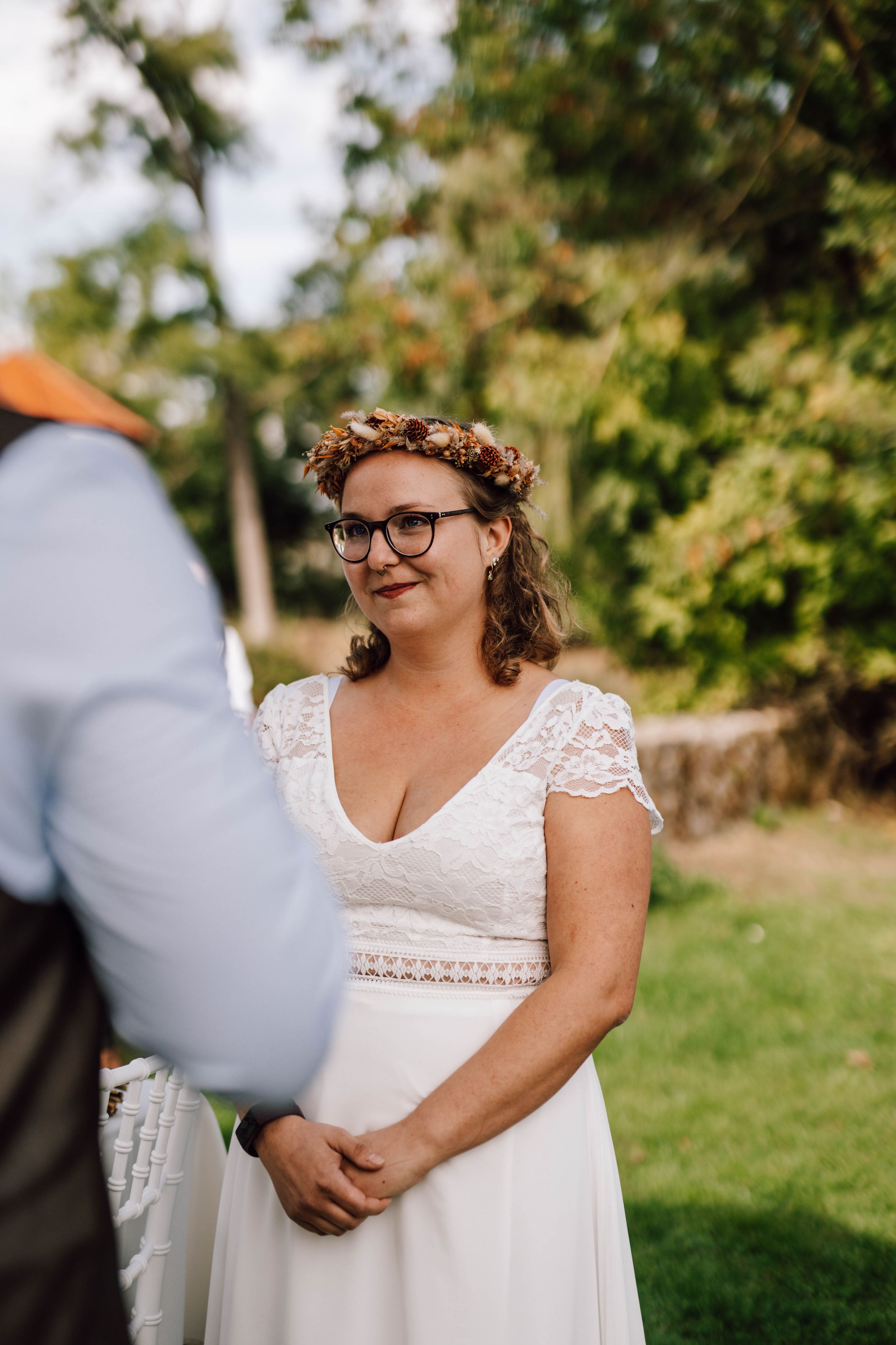 Outdoor wedding ceremony with white lace dress and floral crown against natural backdrop.