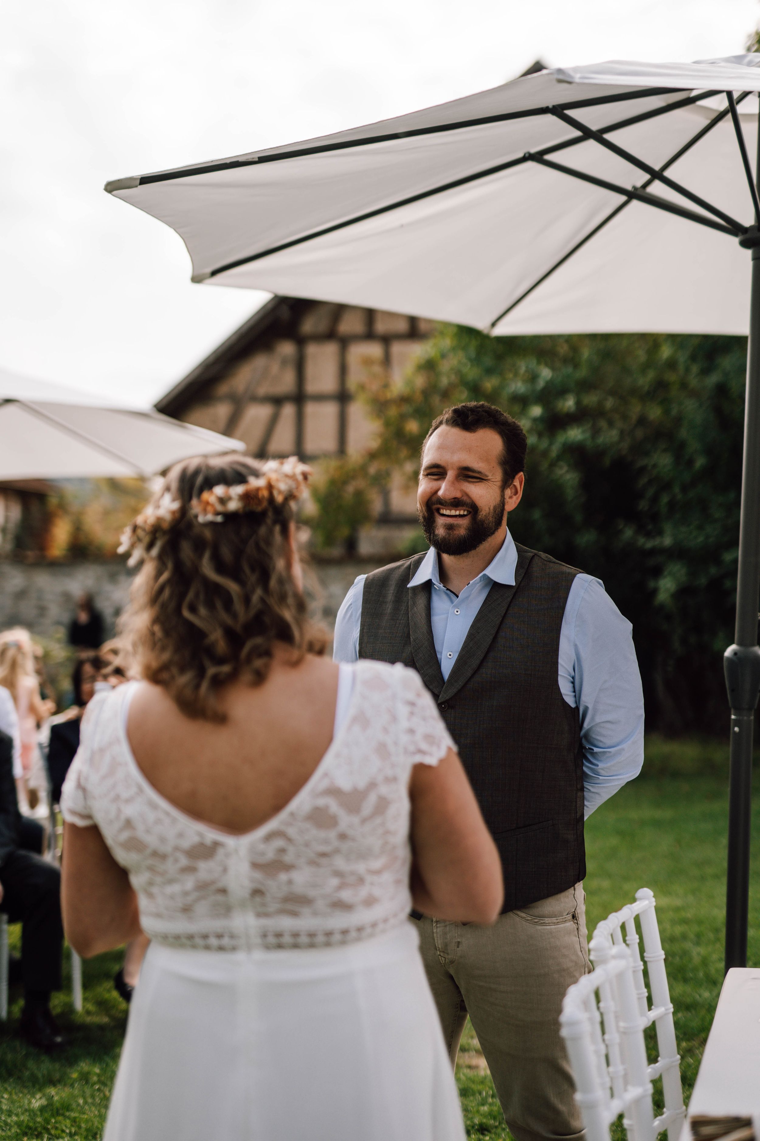 Outdoor wedding ceremony under white umbrellas with stone building backdrop.