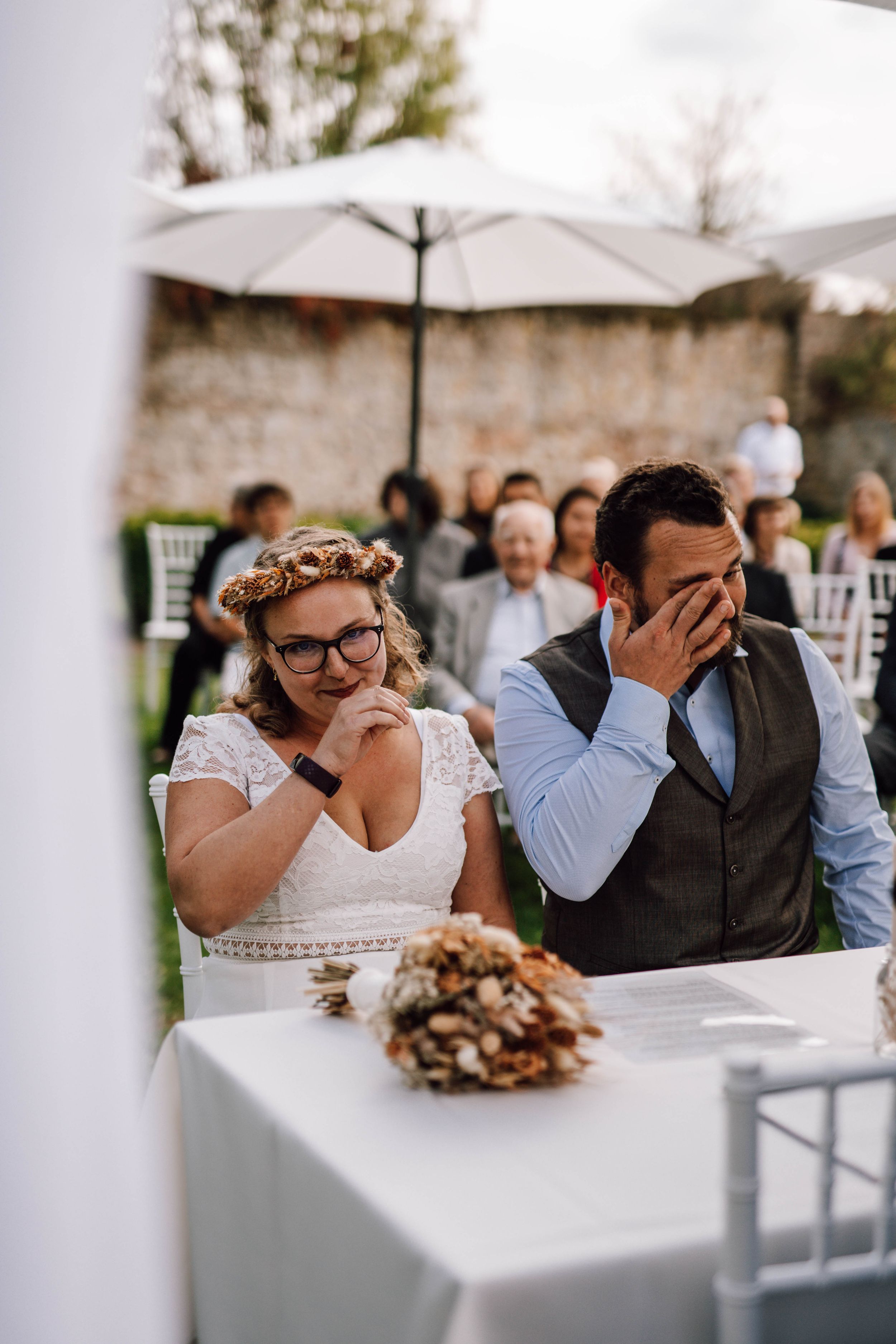 Emotional wedding ceremony moment under white umbrellas with guests in background.