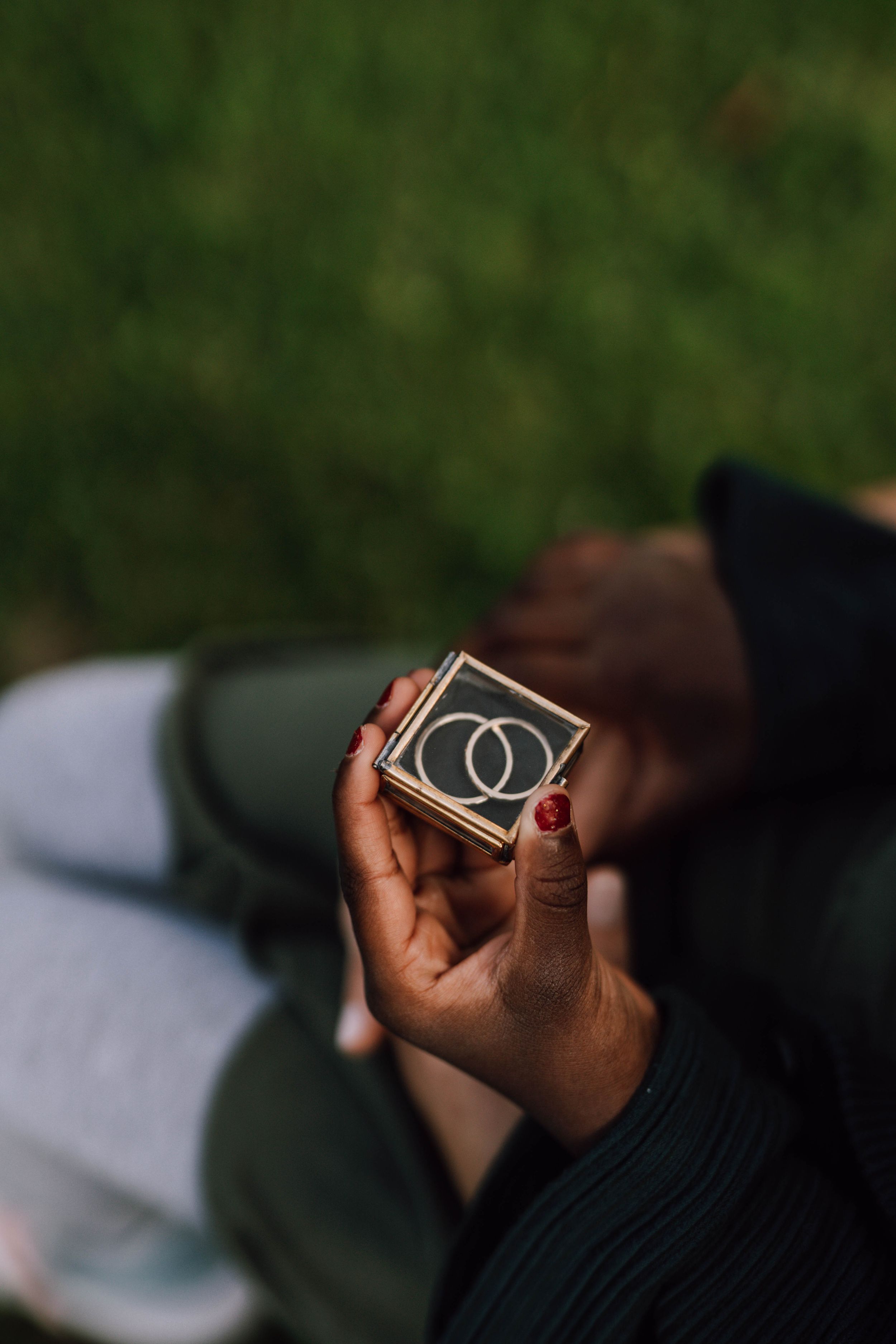 Hands hold a small black box with interlocking ring design against a blurred green background.