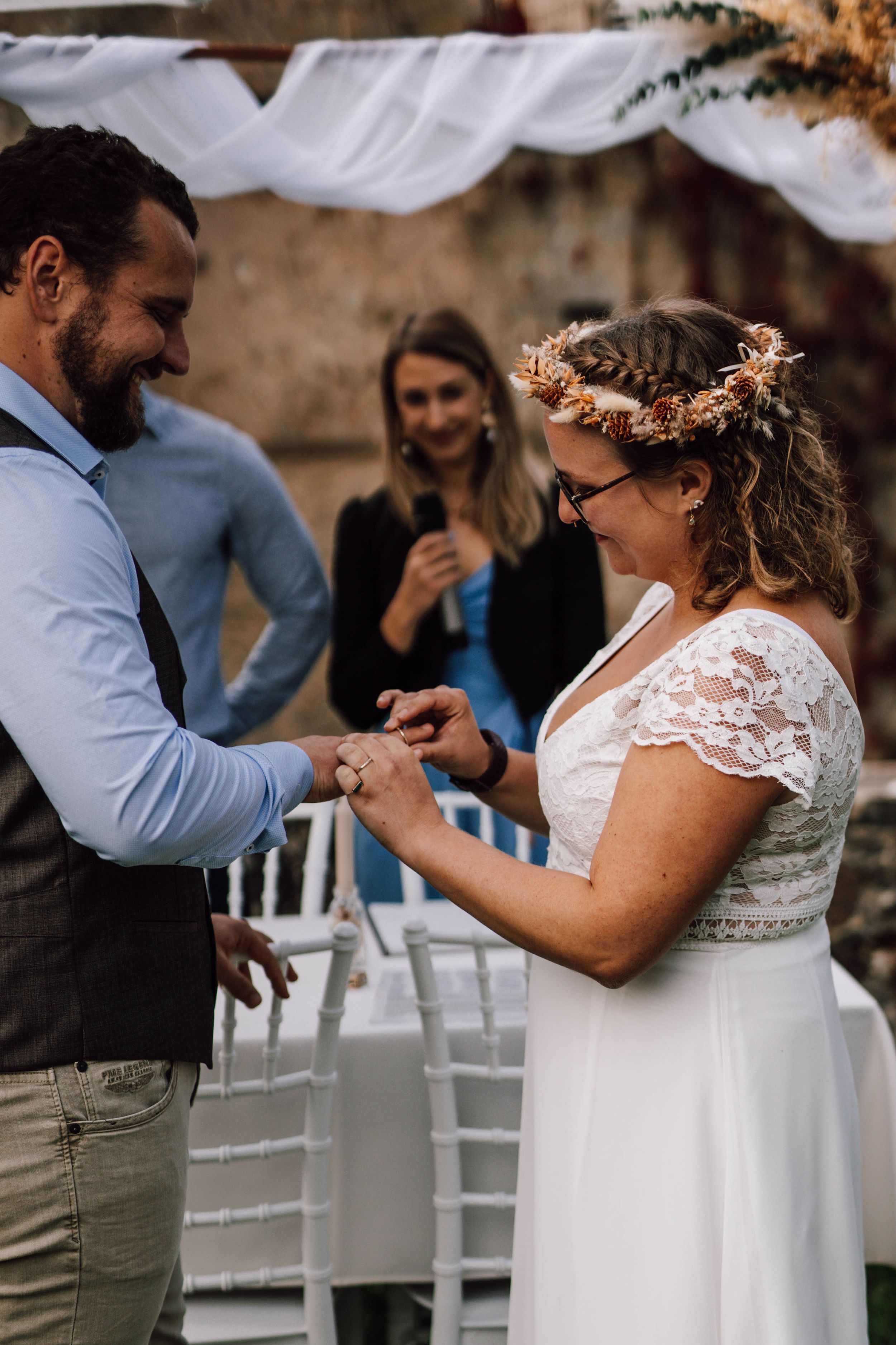 Couple exchanges rings under white fabric canopy during outdoor wedding ceremony.