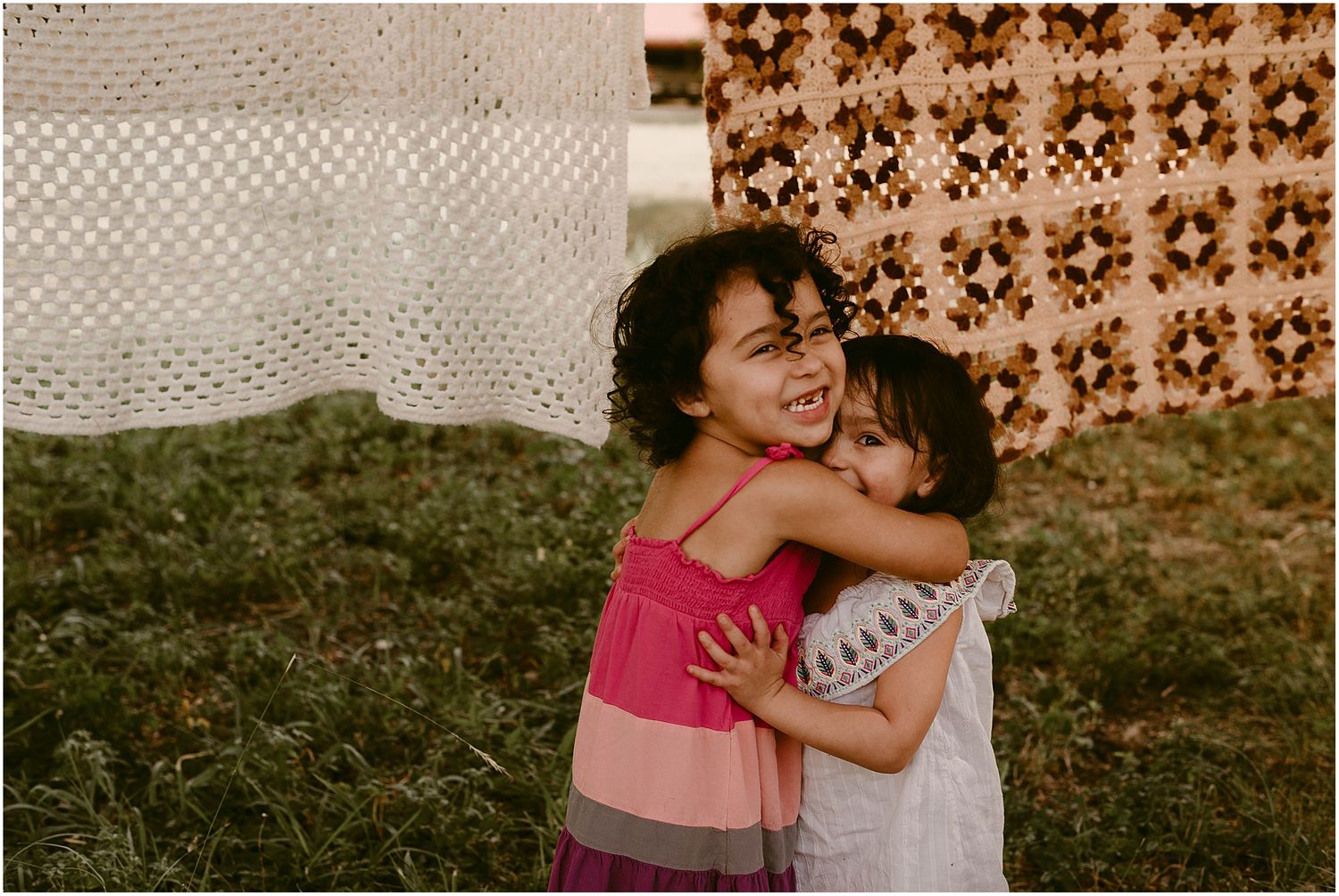 Two children sharing a joyful embrace outdoors with patterned textiles in background.