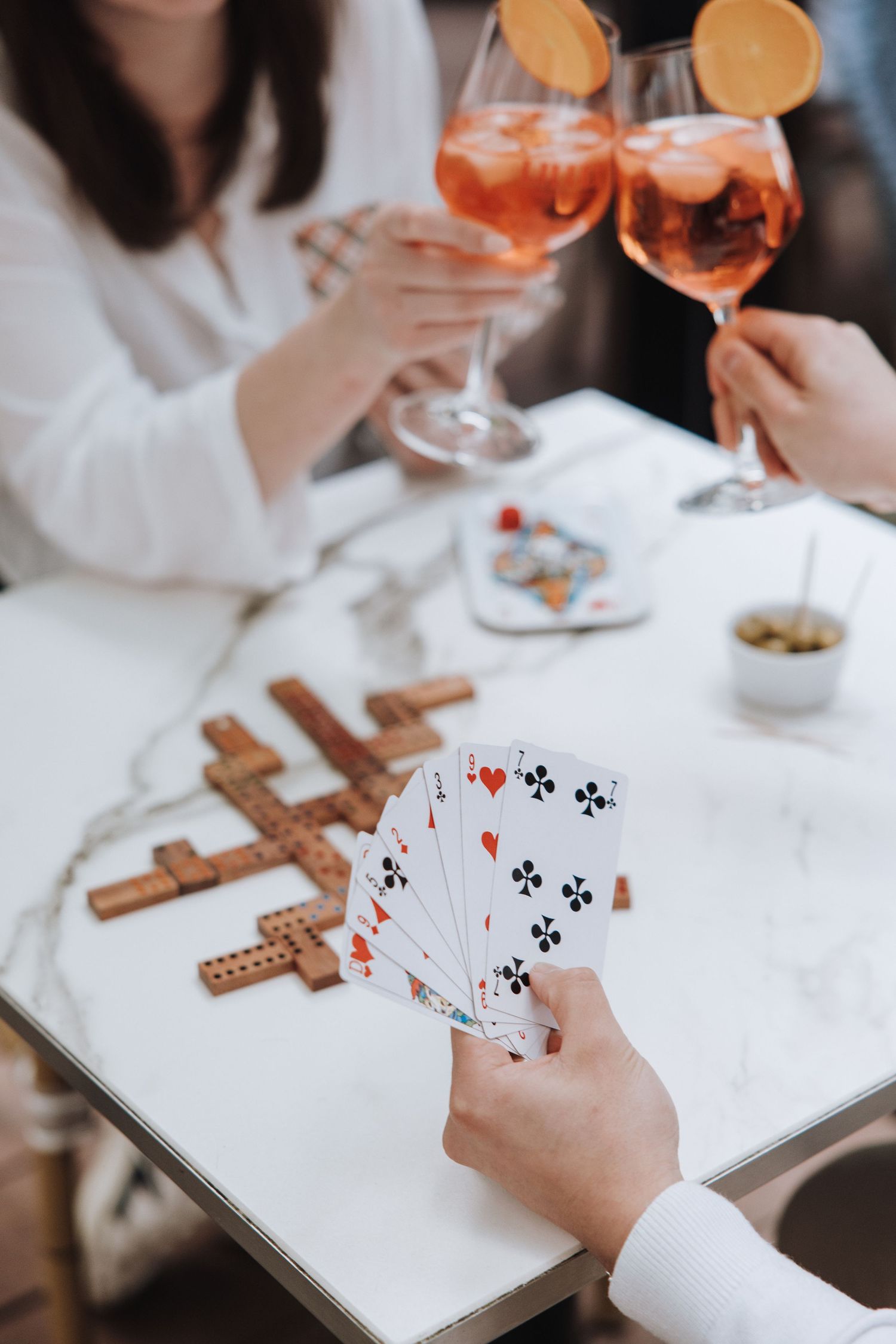White table setting with playing cards, dominoes and orange cocktails for casual game night.
