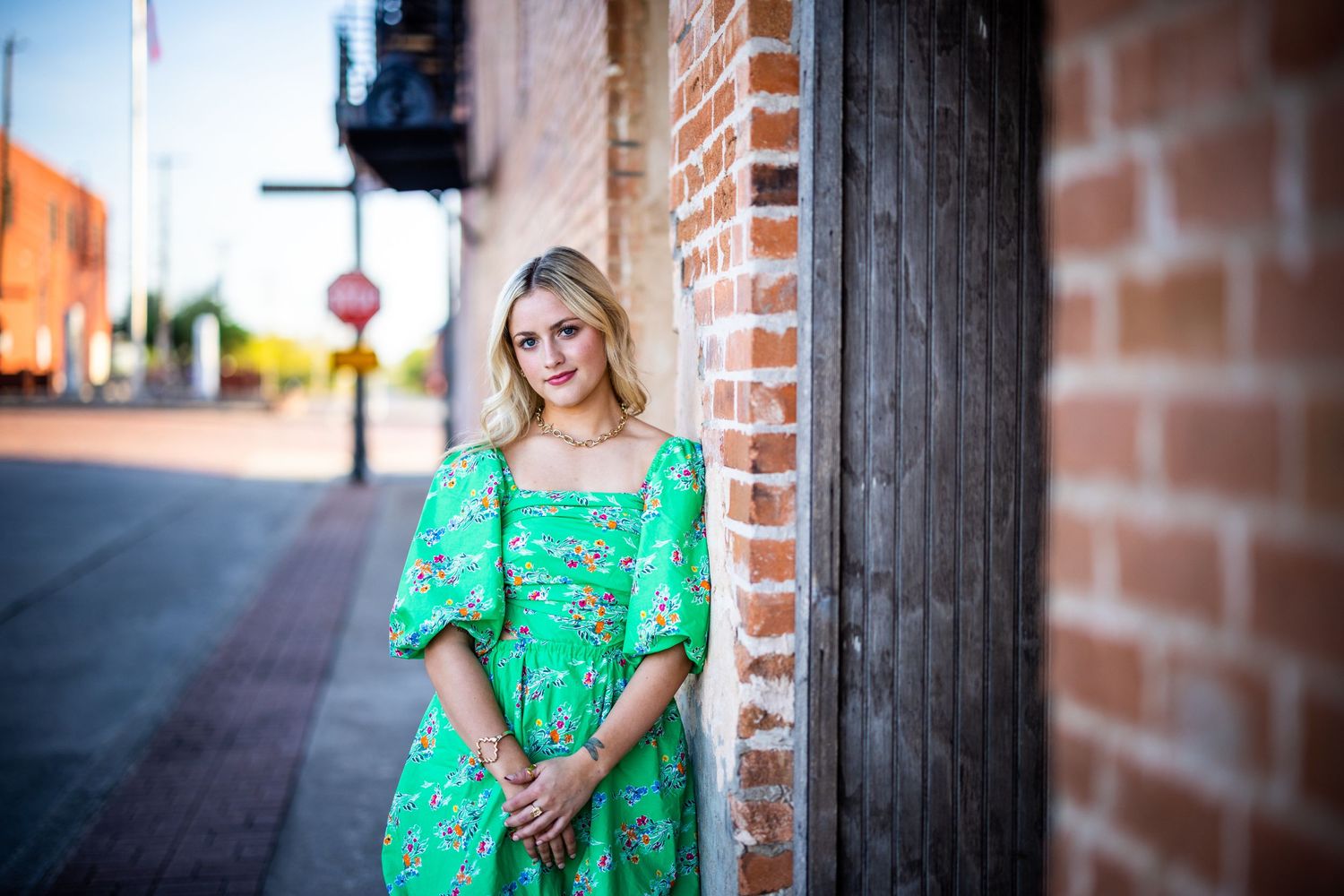 Portrait against brick wall with vintage style green floral dress in urban setting.