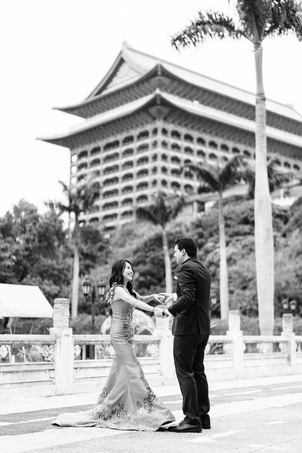 A couple dances in black and white photography with an Asian architectural landmark in the background.