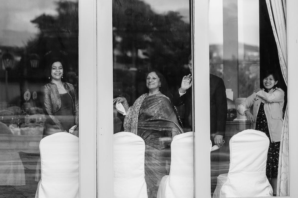 Wedding party members wave through glass windows beside white chairs.