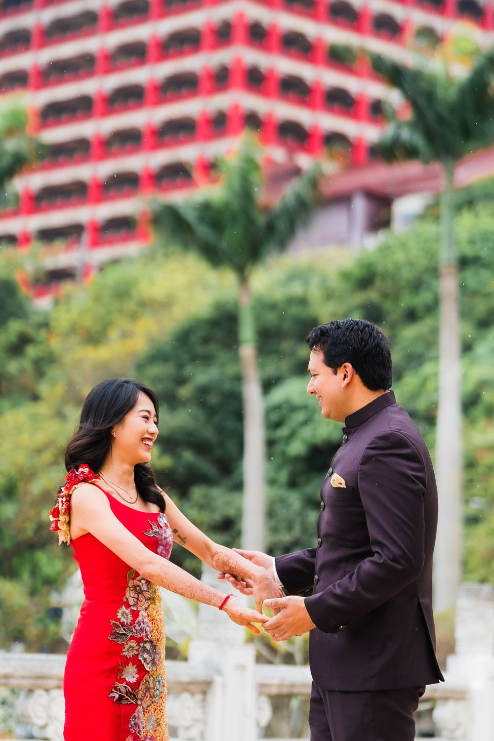 A couple shares a joyful moment while holding hands in front of a grand Asian building.