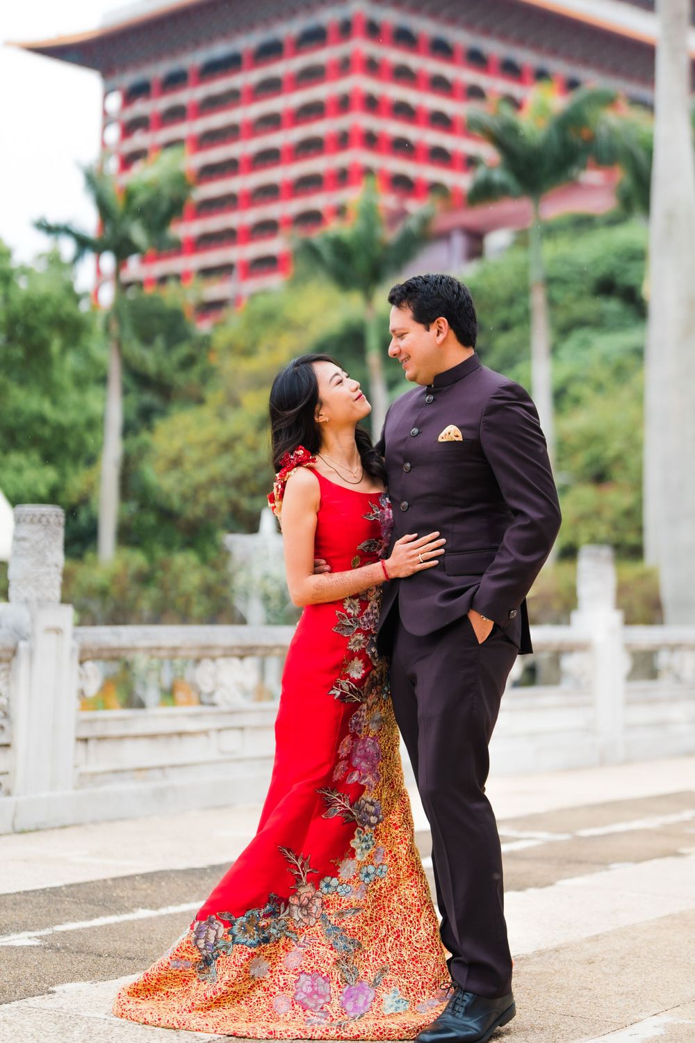 Romantic moment captured in front of a red pagoda-style building with palm trees.