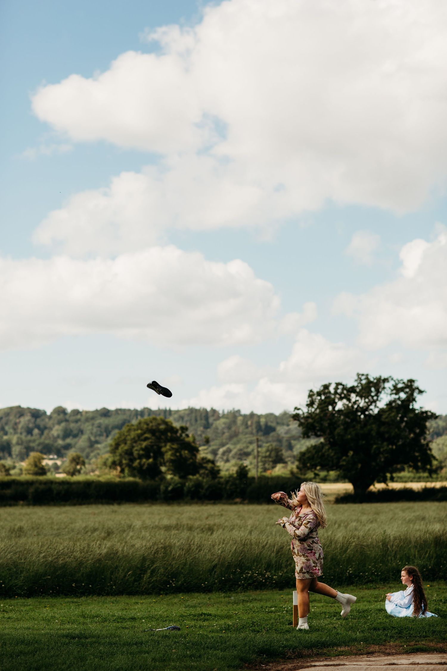 Someone tosses an object into the air against a pastoral landscape with rolling hills.