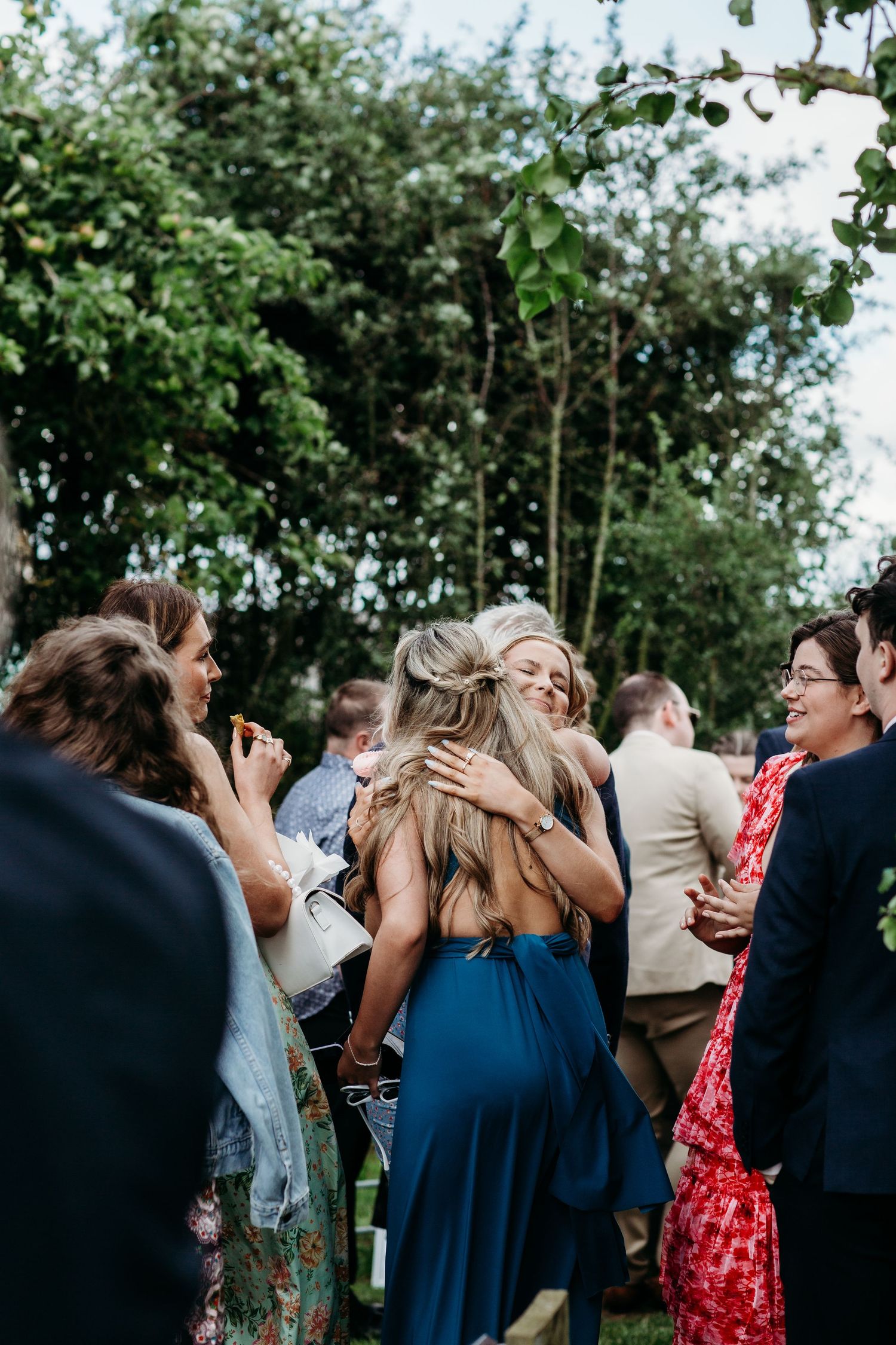 Wedding guests mingle and embrace at an outdoor garden reception.