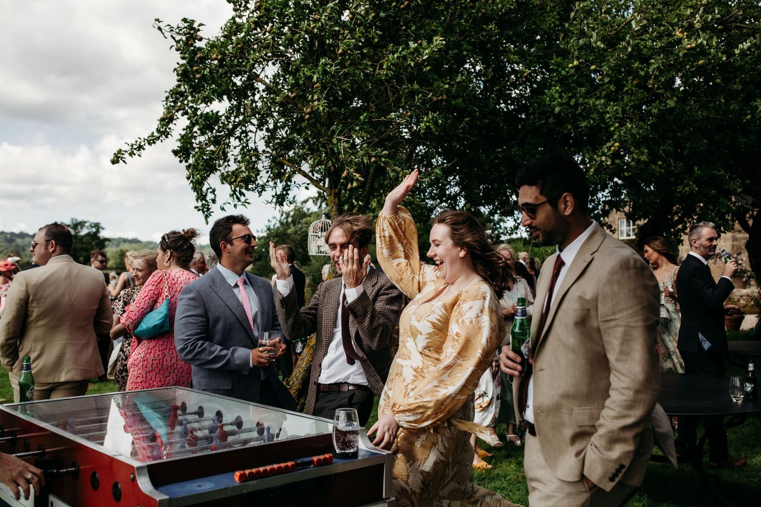 Guests gather around DJ equipment at an outdoor party under tree branches.