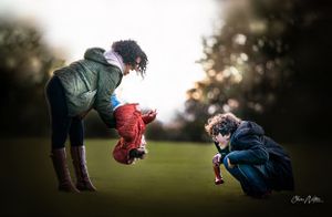 Two photographers crouching low in a grassy field during golden hour to capture creative shots at sunset.