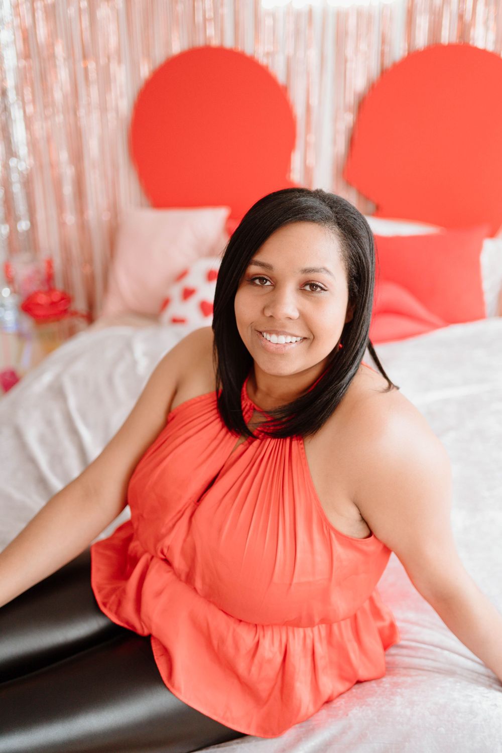 Lifestyle portrait with coral halter top against pink and red heart-shaped backdrop.