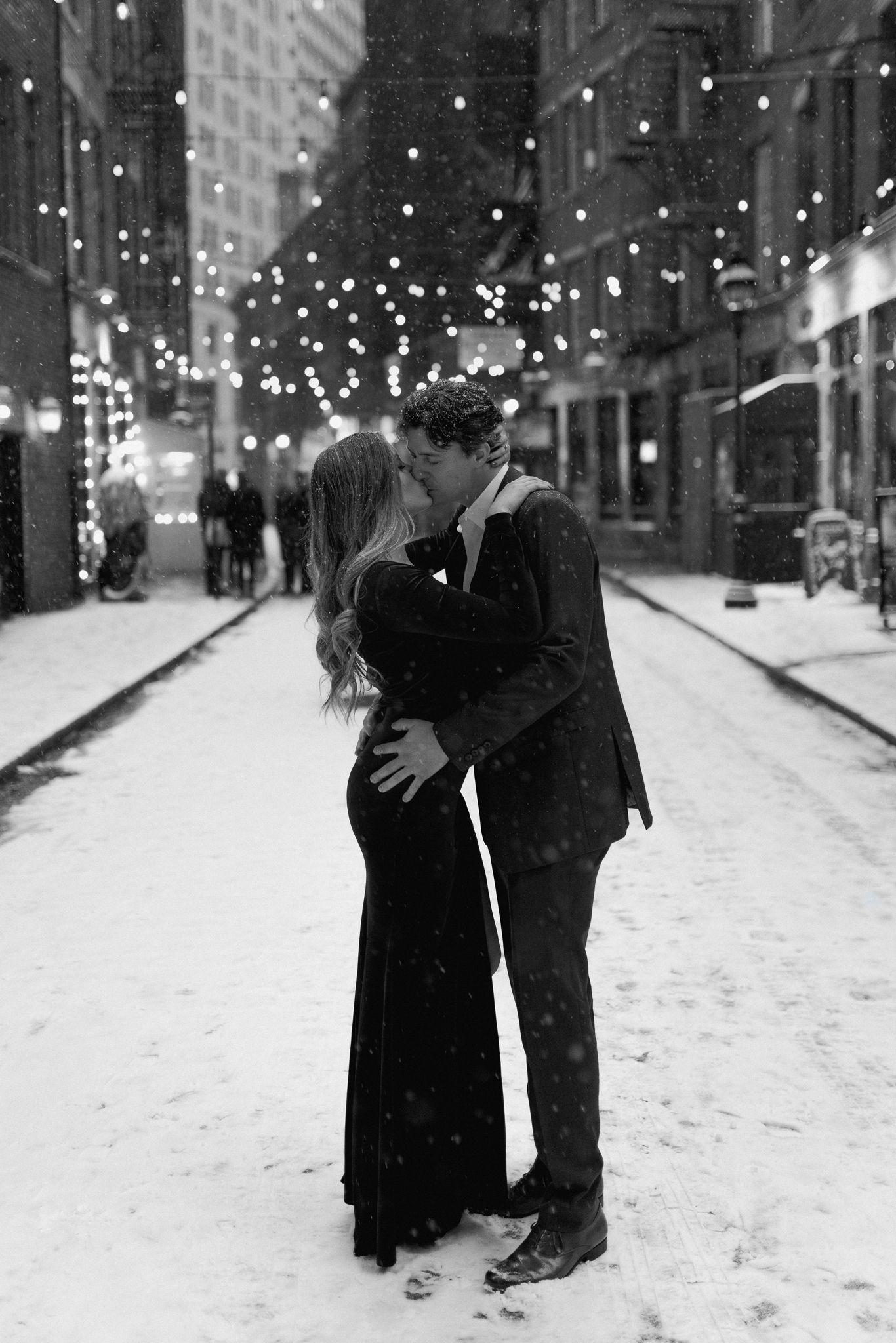 A romantic embrace on a snow-covered street illuminated by overhead lights.