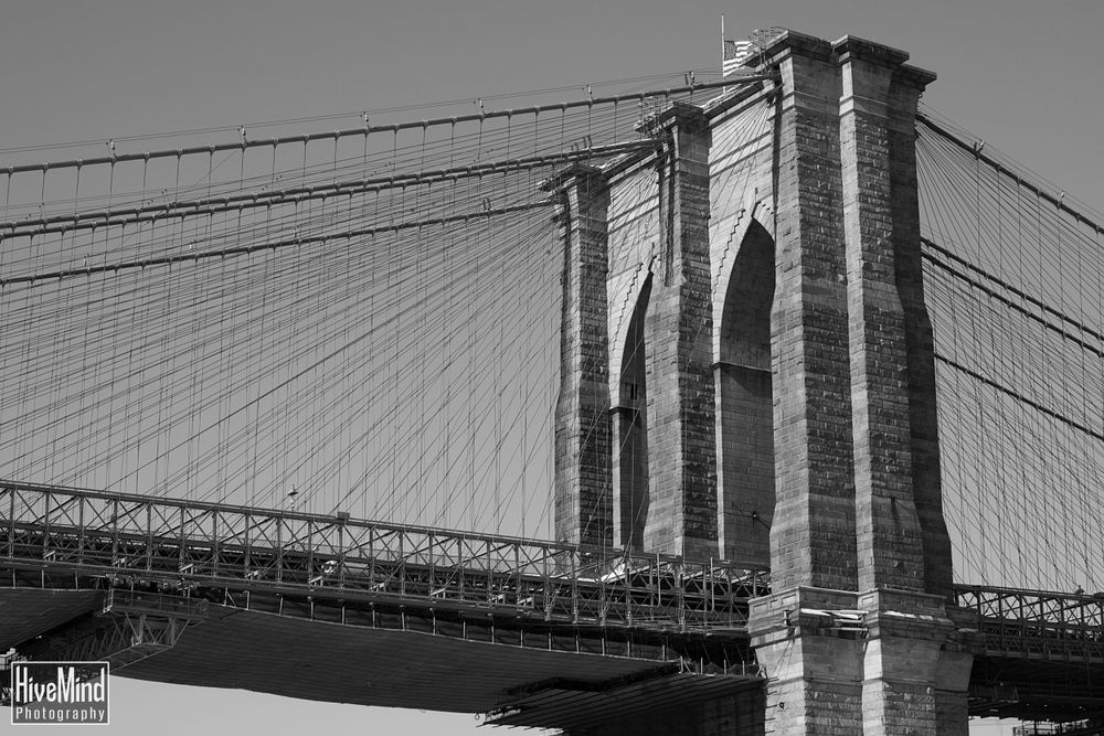 Black and white architectural photograph of the Brooklyn Bridge against a clear sky.