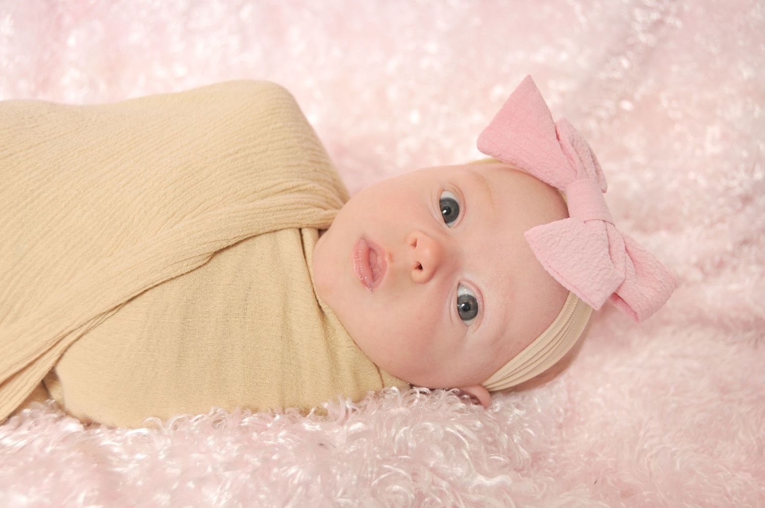 Newborn baby girl on fluffy pink background wrapped in neutral tones