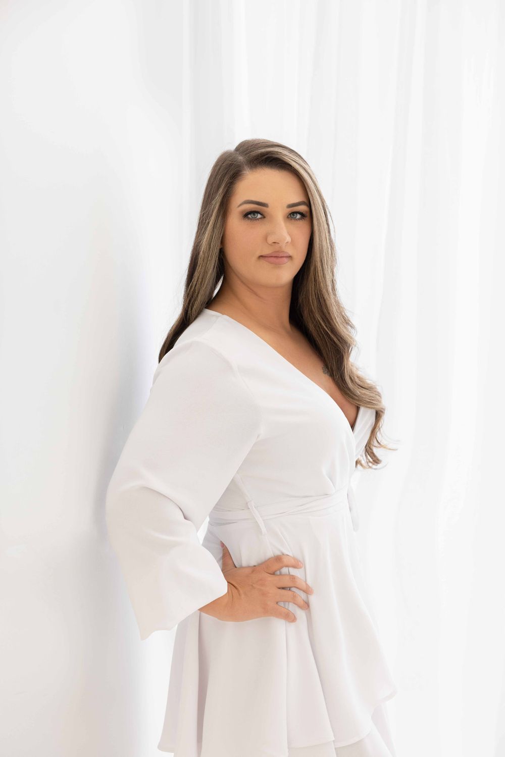 Elegant portrait in white wrap dress against light backdrop.