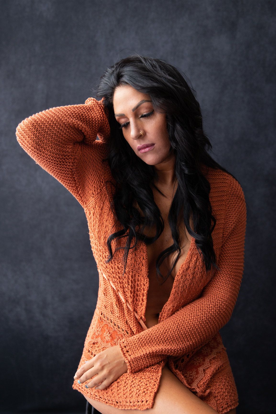 Sensual portrait in orange knit sweater against dark studio backdrop.