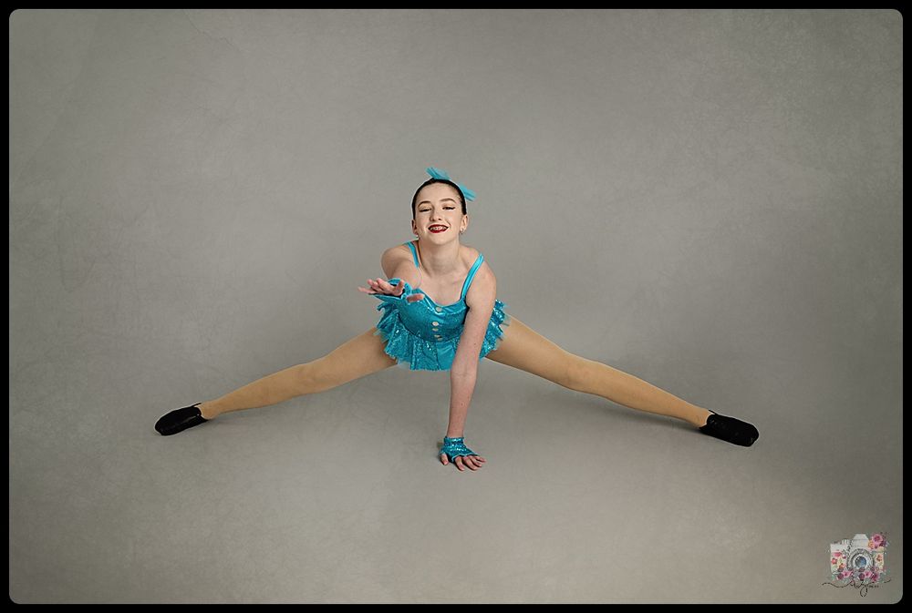 A dancer in a turquoise costume performs a split pose on the floor.