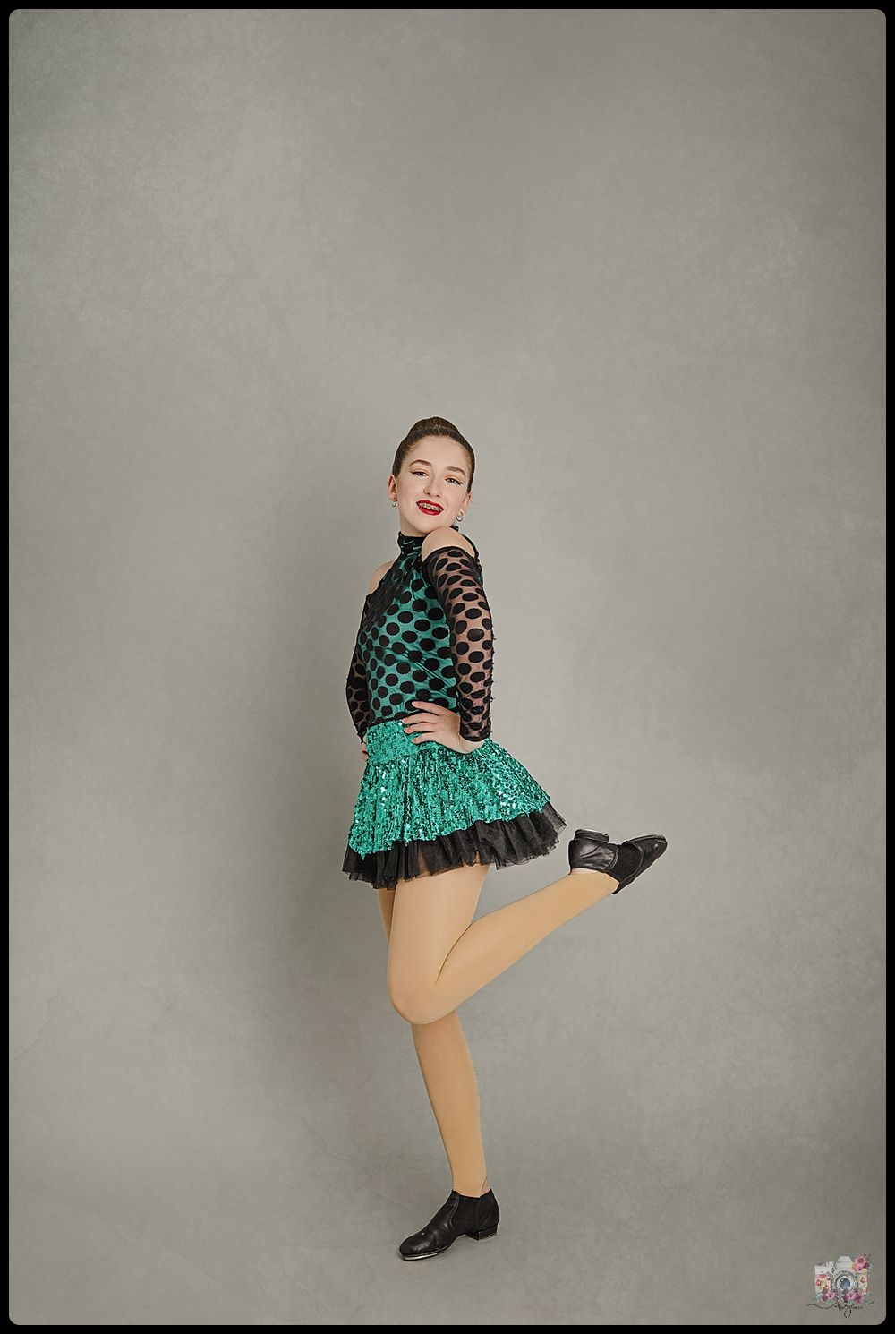 A dancer in a green and black outfit strikes a playful pose against a gray background.