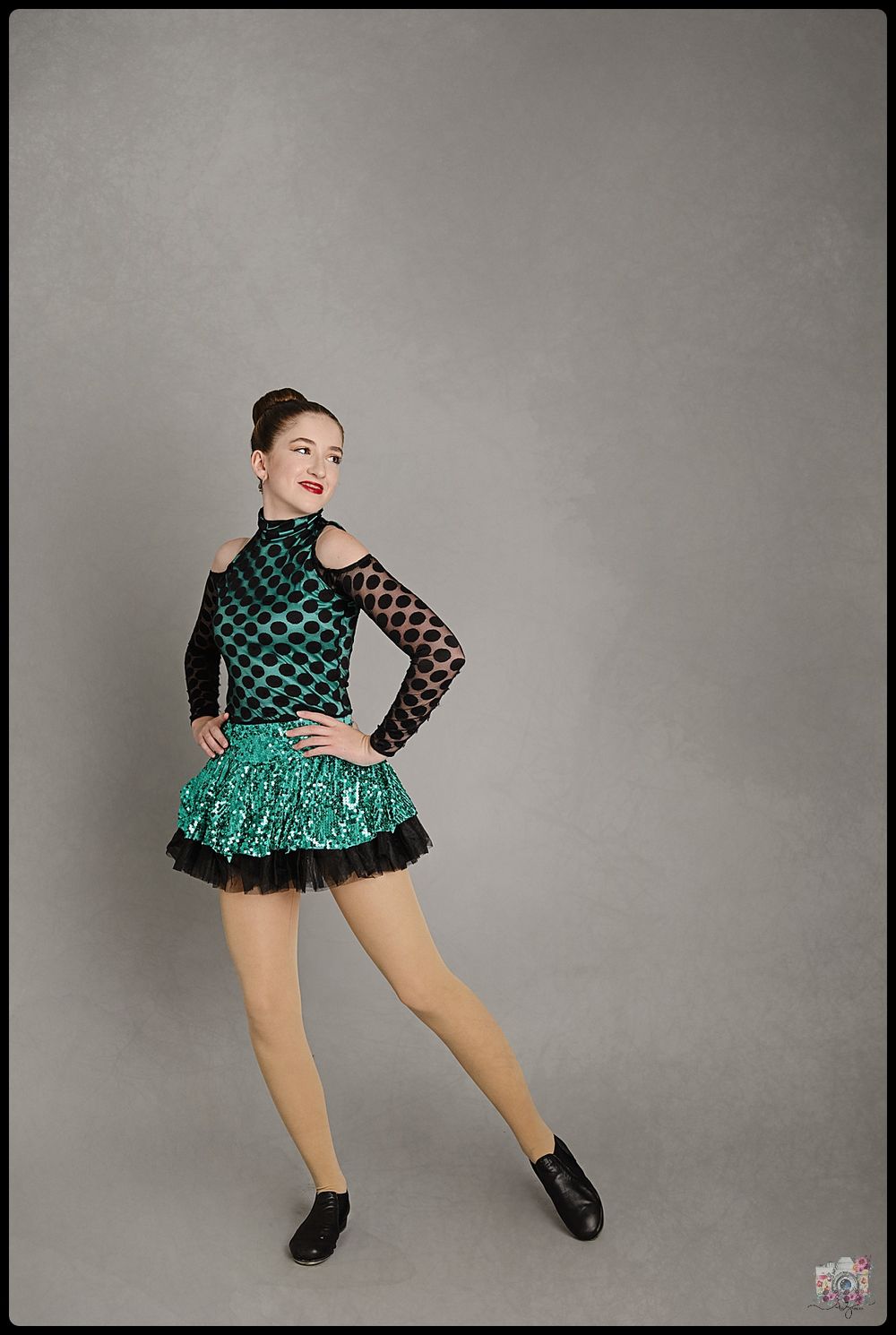 A dancer in a green and black costume poses with one leg raised against a gray backdrop.