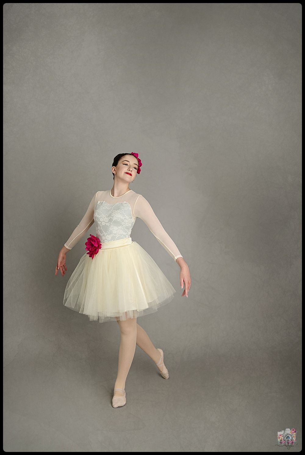 A ballerina in a white tutu with a pink flower performs a graceful pose.