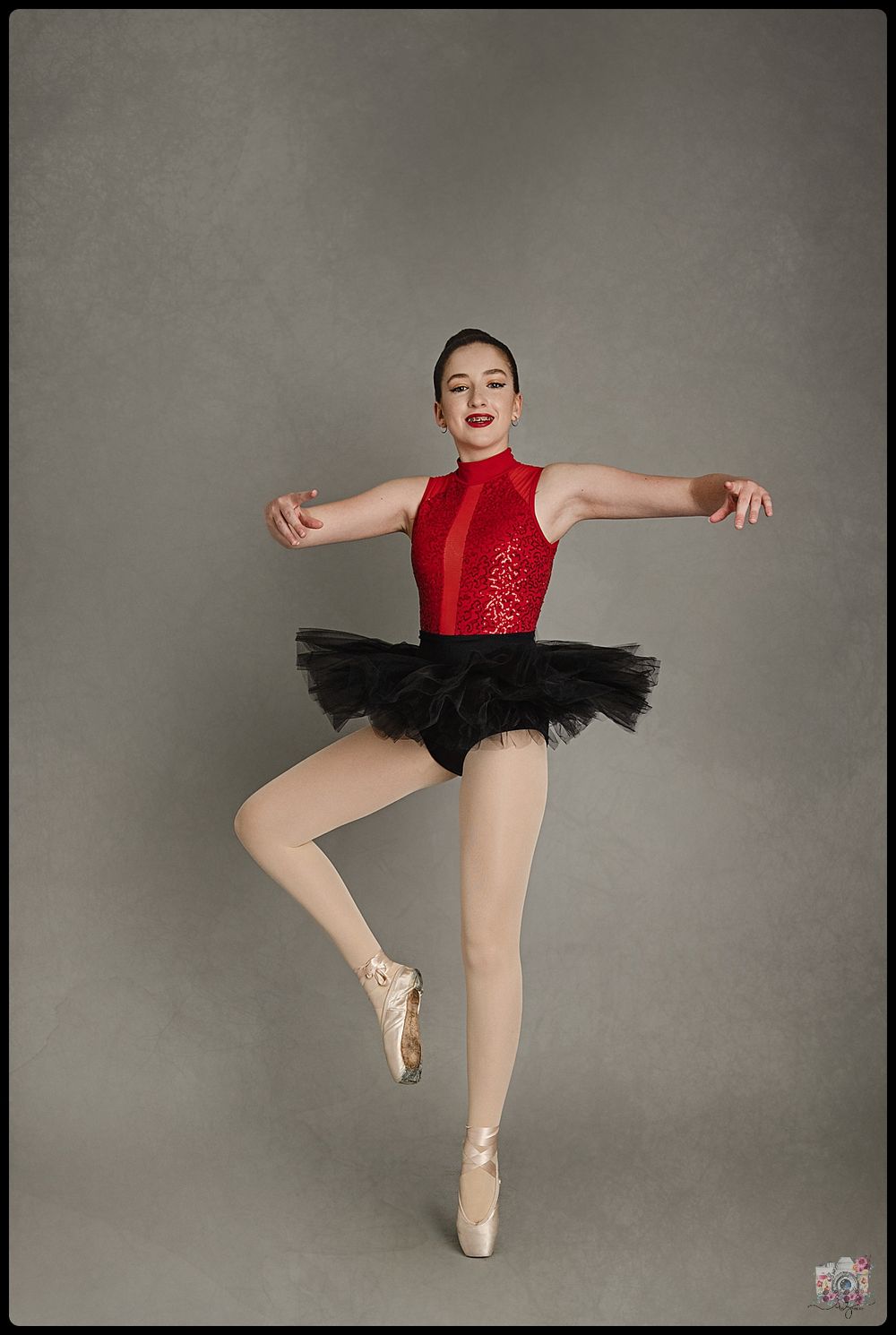 Dancer wearing red sequined leotard and black tutu performs ballet pose on pointe.