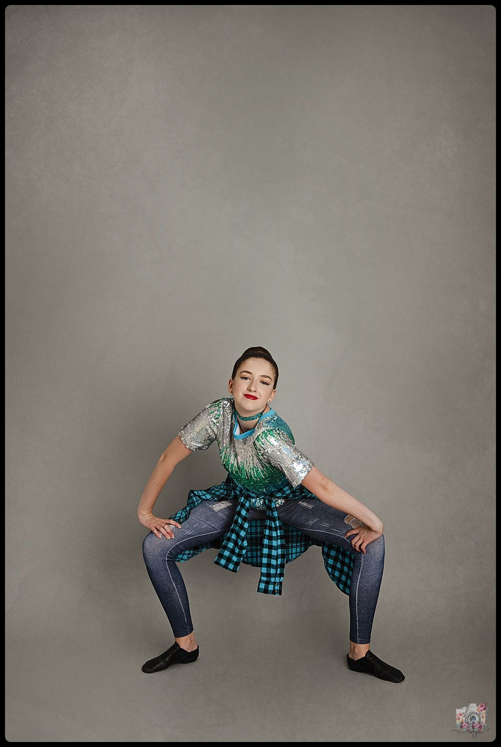 Performer in teal shirt and jeans strikes dynamic pose against grey background.