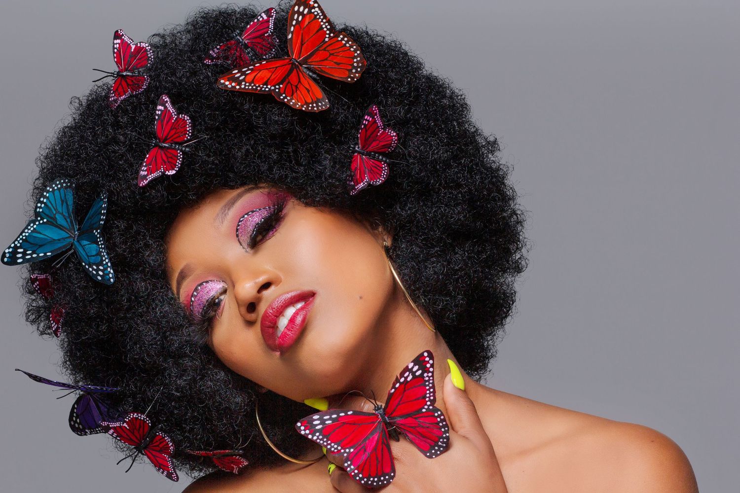 Creative beauty portrait with afro hairstyle decorated with red and blue butterflies.