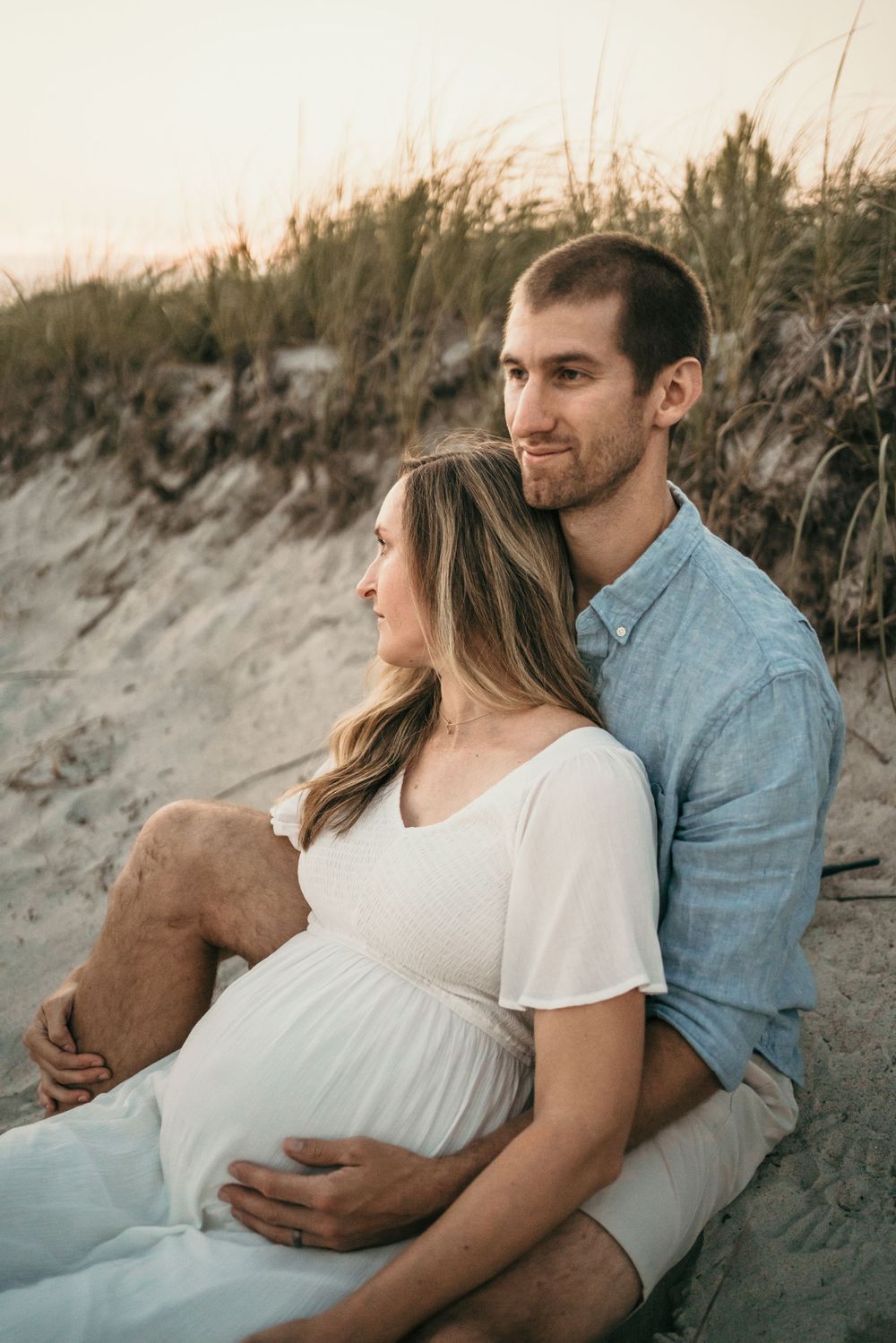 Expecting couple shares intimate moment on sandy beach at sunset.
