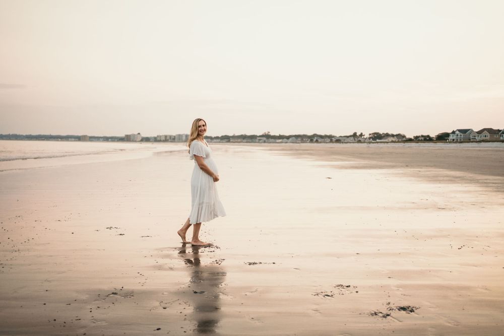 Woman in white dress twirls on empty beach during sunset.