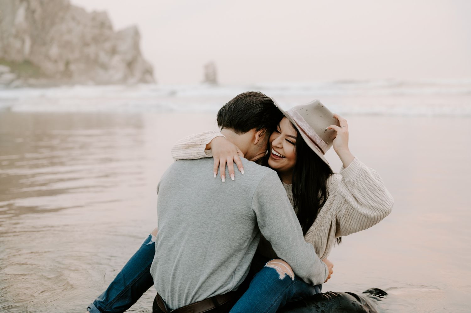 Couple shares tender moment on rocky beach at sunset.