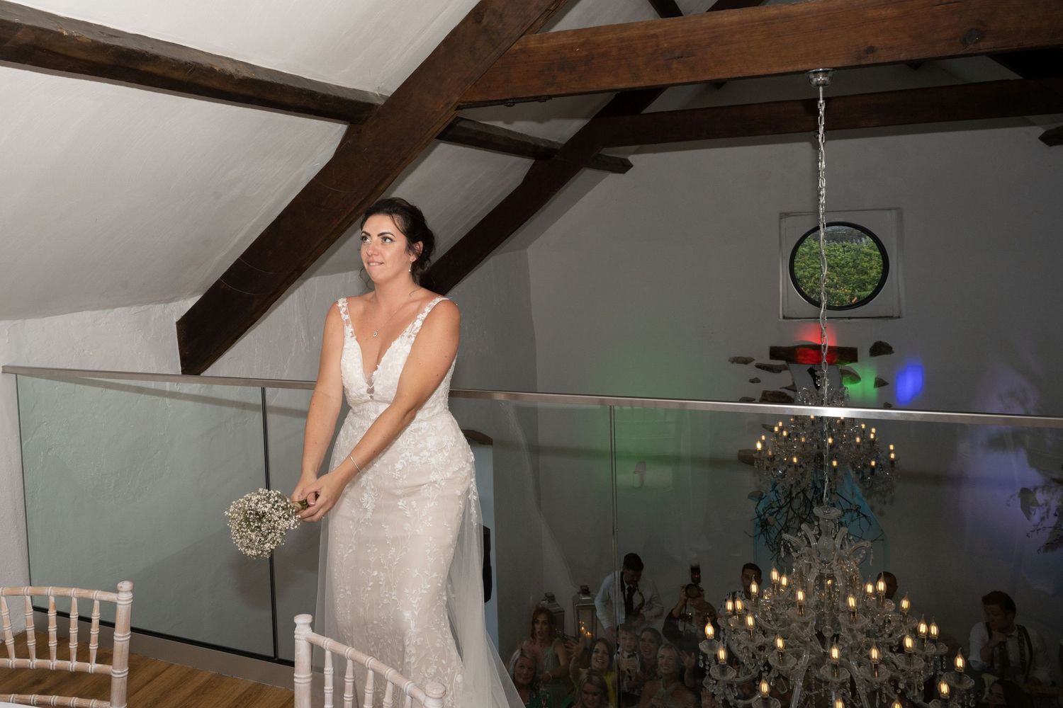 An elegant wedding scene featuring exposed wooden beams, crystal chandeliers and modern glass railings.