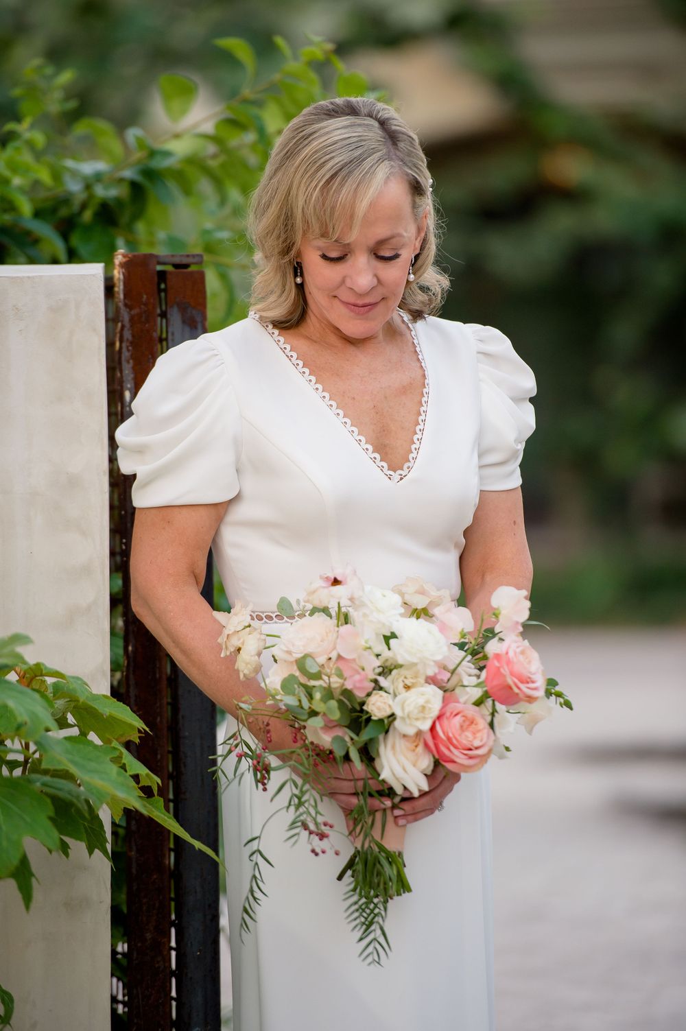 Close-up of bride holding delicate pink and white floral bouquet against garden greenery. Commodore Perry Estate Wedding