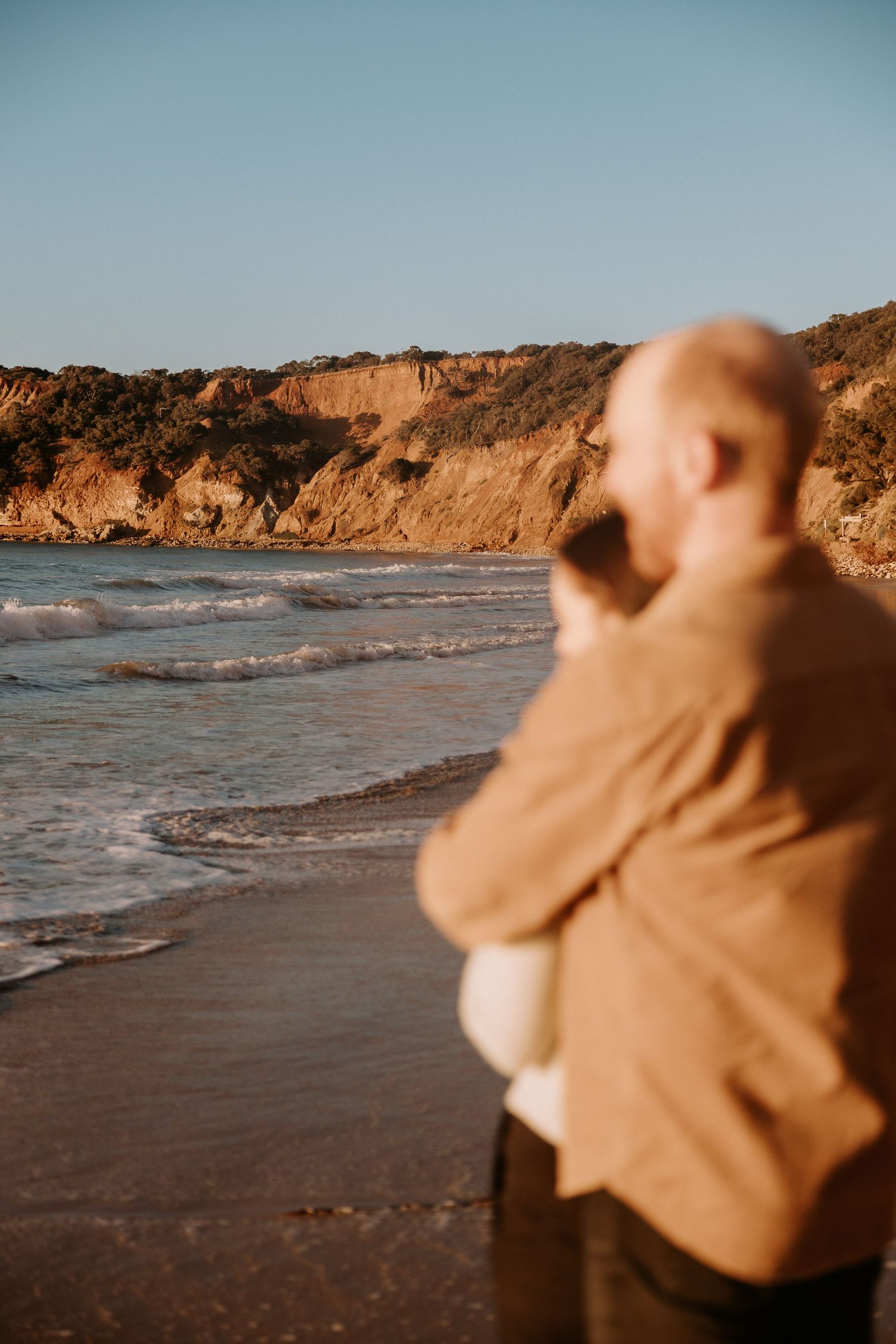 Person admiring the scenic coastal view with cliffs and ocean waves at sunset.
