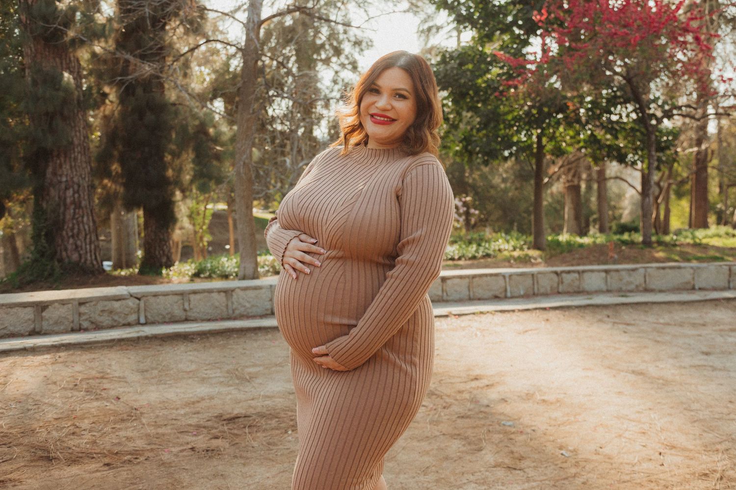 Maternity portrait in ribbed beige dress at sunset in park setting.